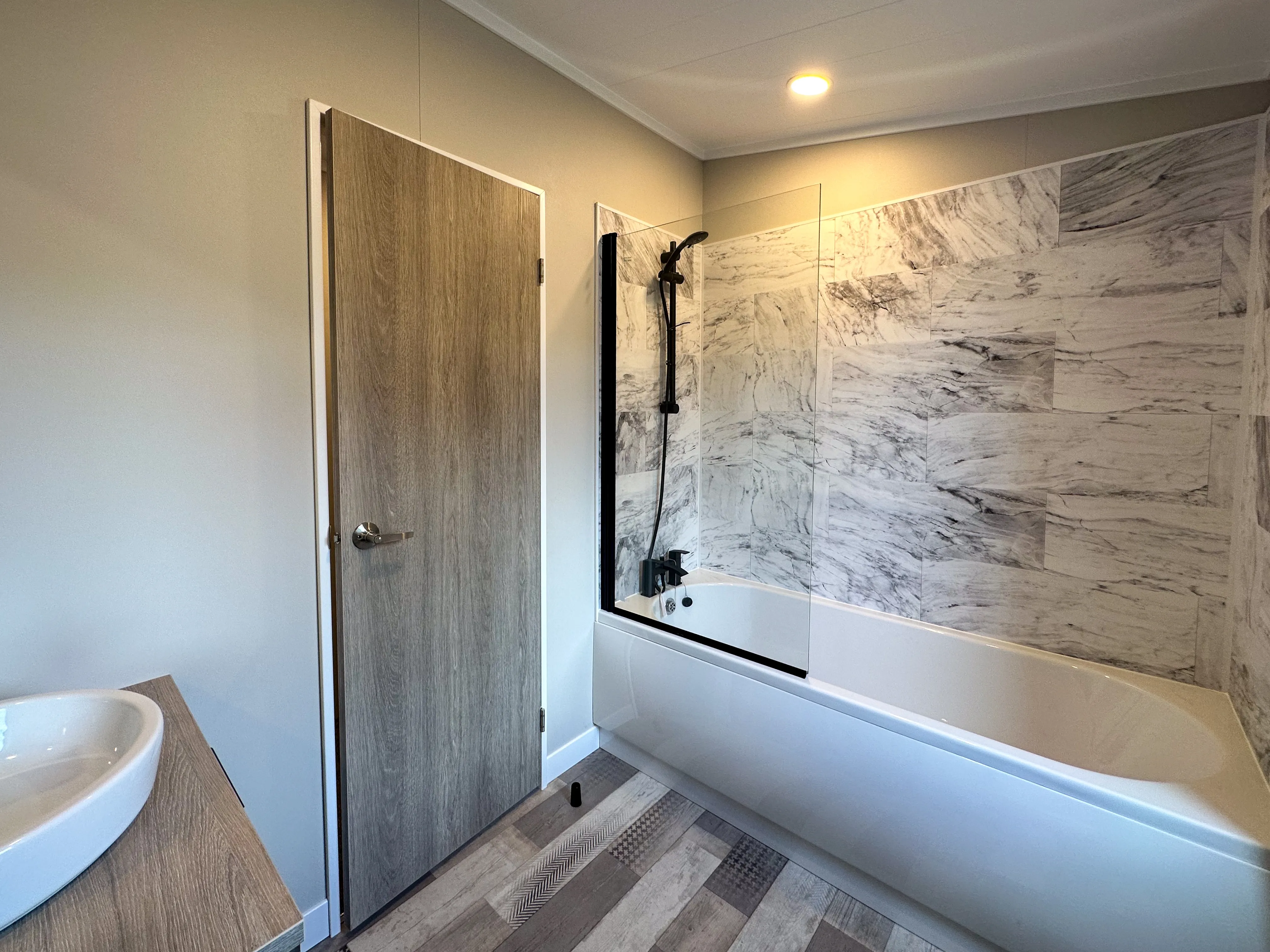 Modern bathroom with a bath-shower combo, glass screen and marble-effect wall tiles