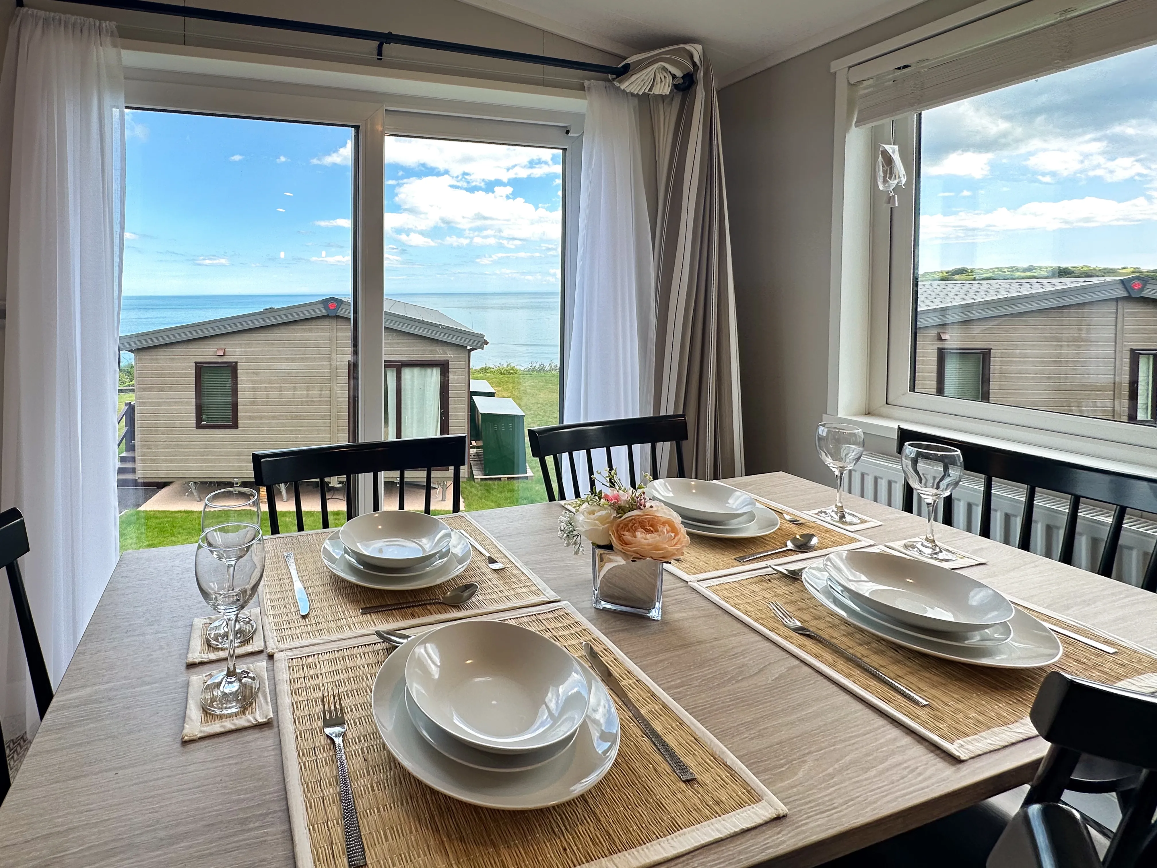 Set dining table by large windows with sea view beyond holiday lodges