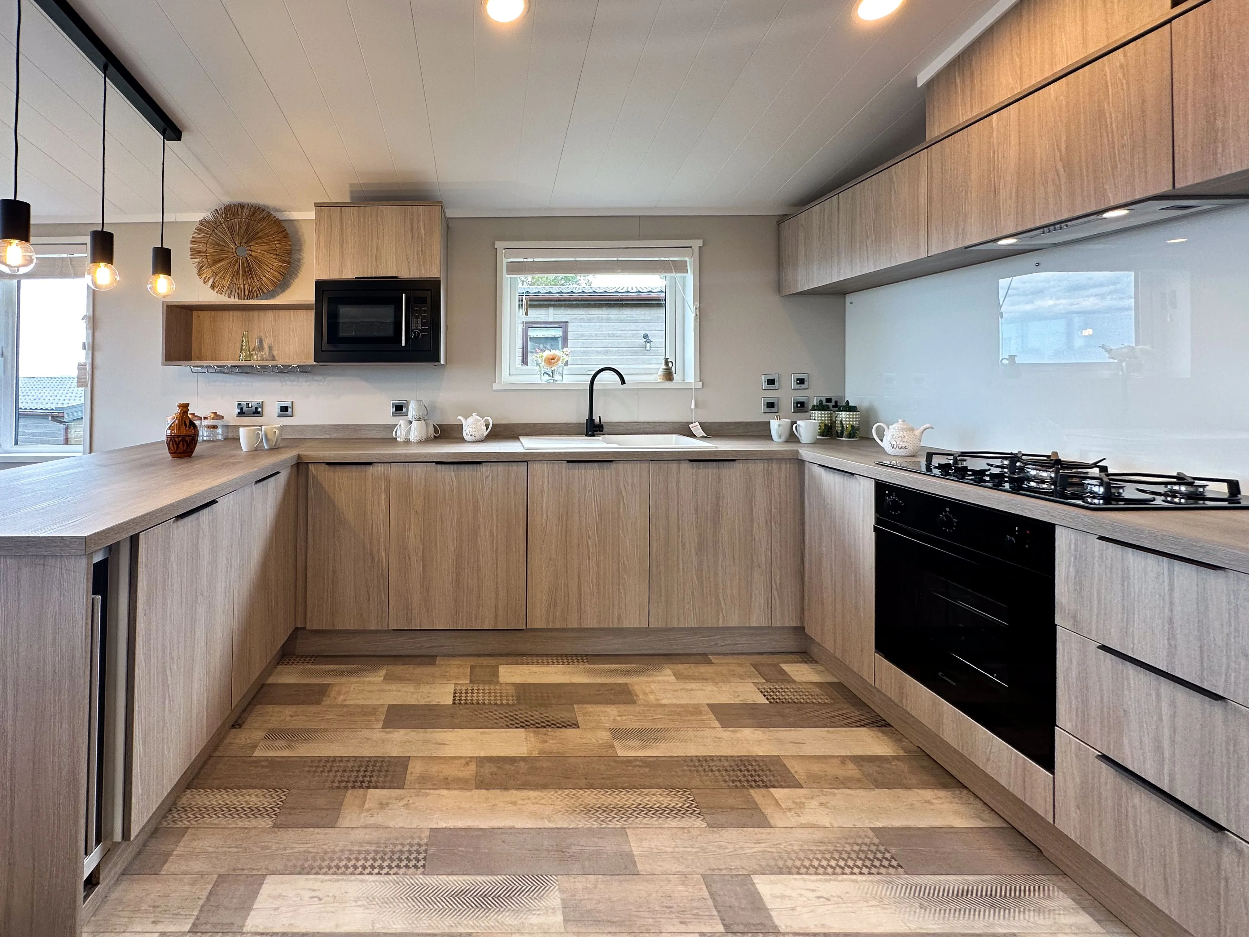 Modern U-shaped kitchen with light wood cabinets, black oven and hob, and pendant lights over a grey worktop