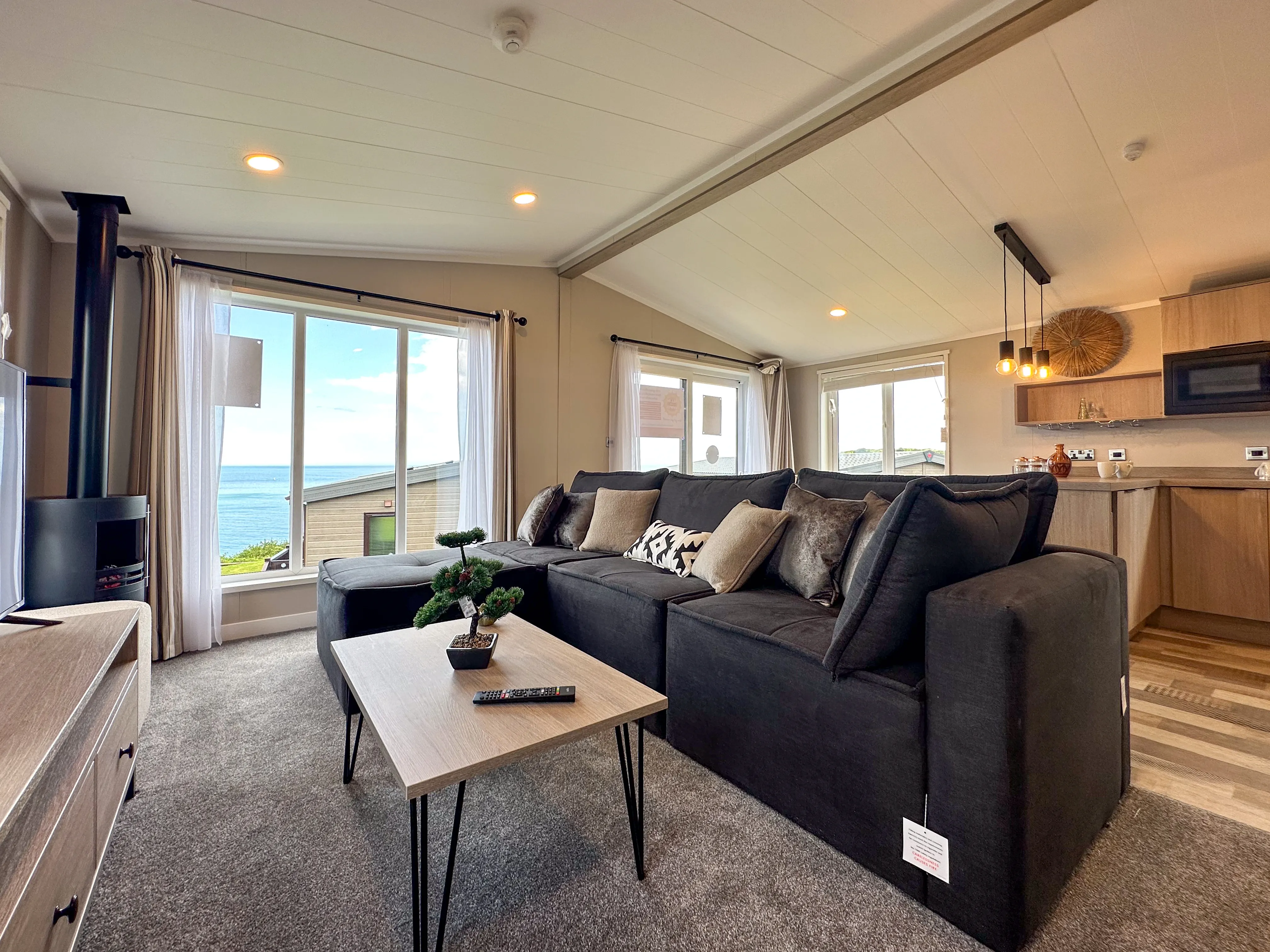 Modern open-plan living room with dark sectional sofa and large windows overlooking the sea