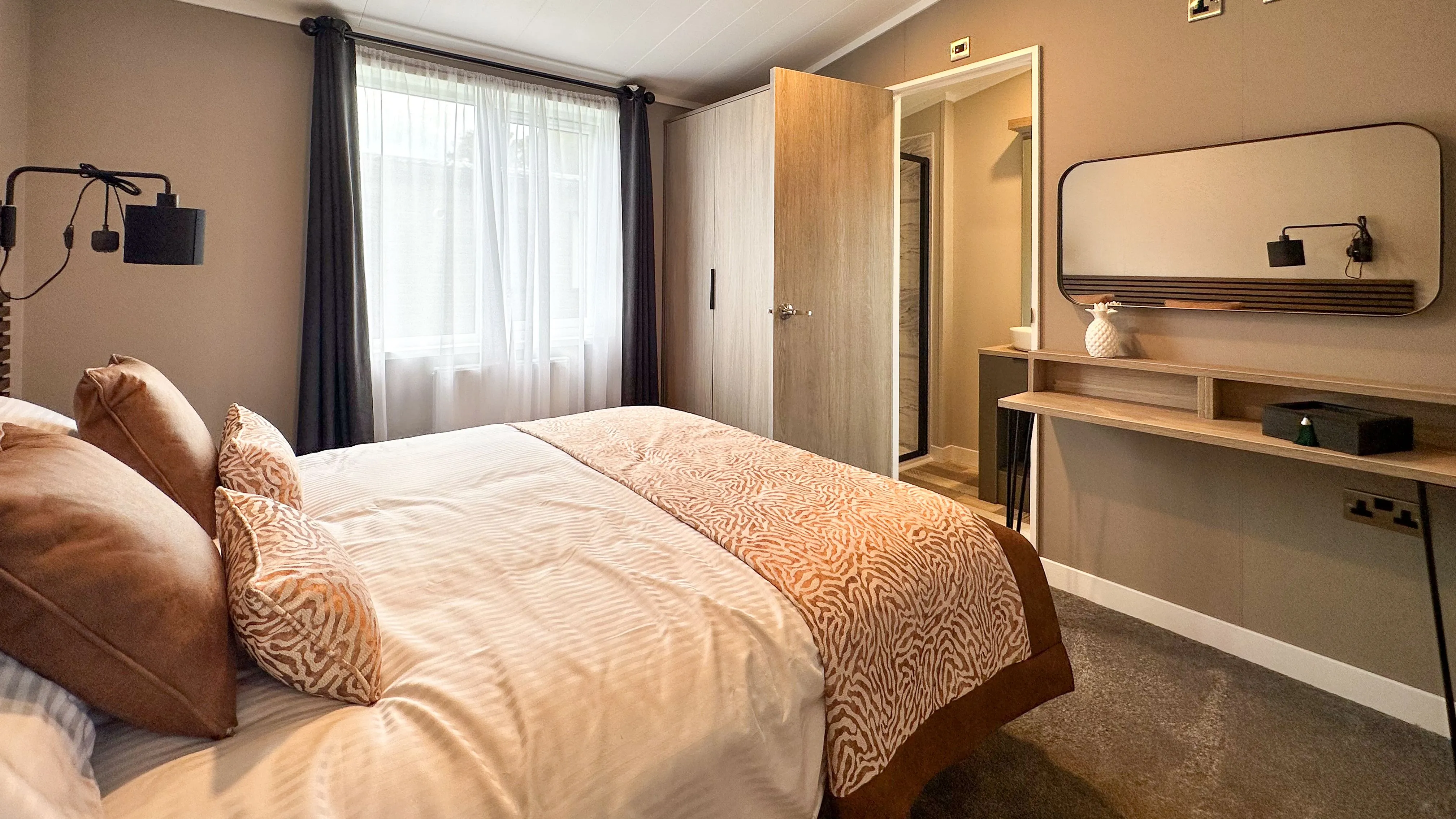 Modern bedroom with double bed, grey walls, window with dark curtains, and vanity desk with mirror