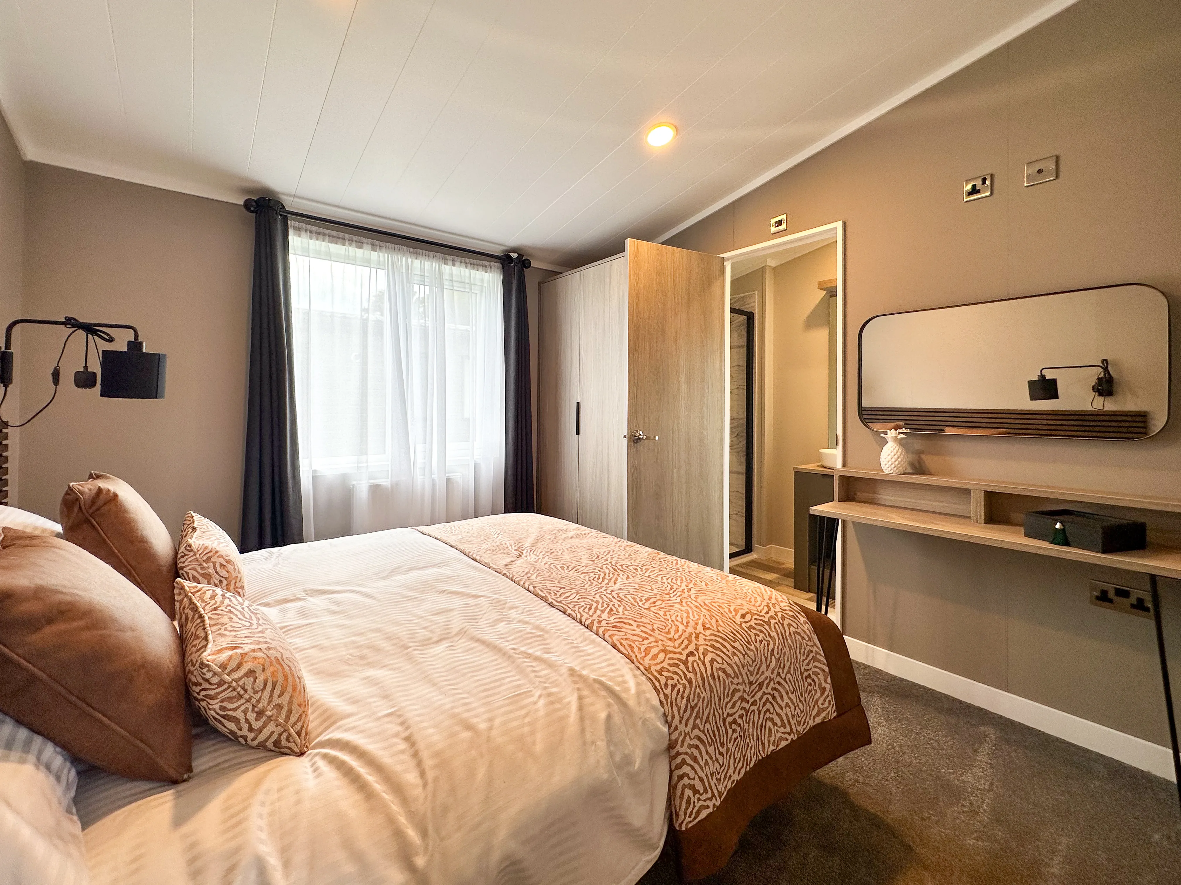 Modern bedroom with double bed, grey walls, window with dark curtains, and vanity desk with mirror