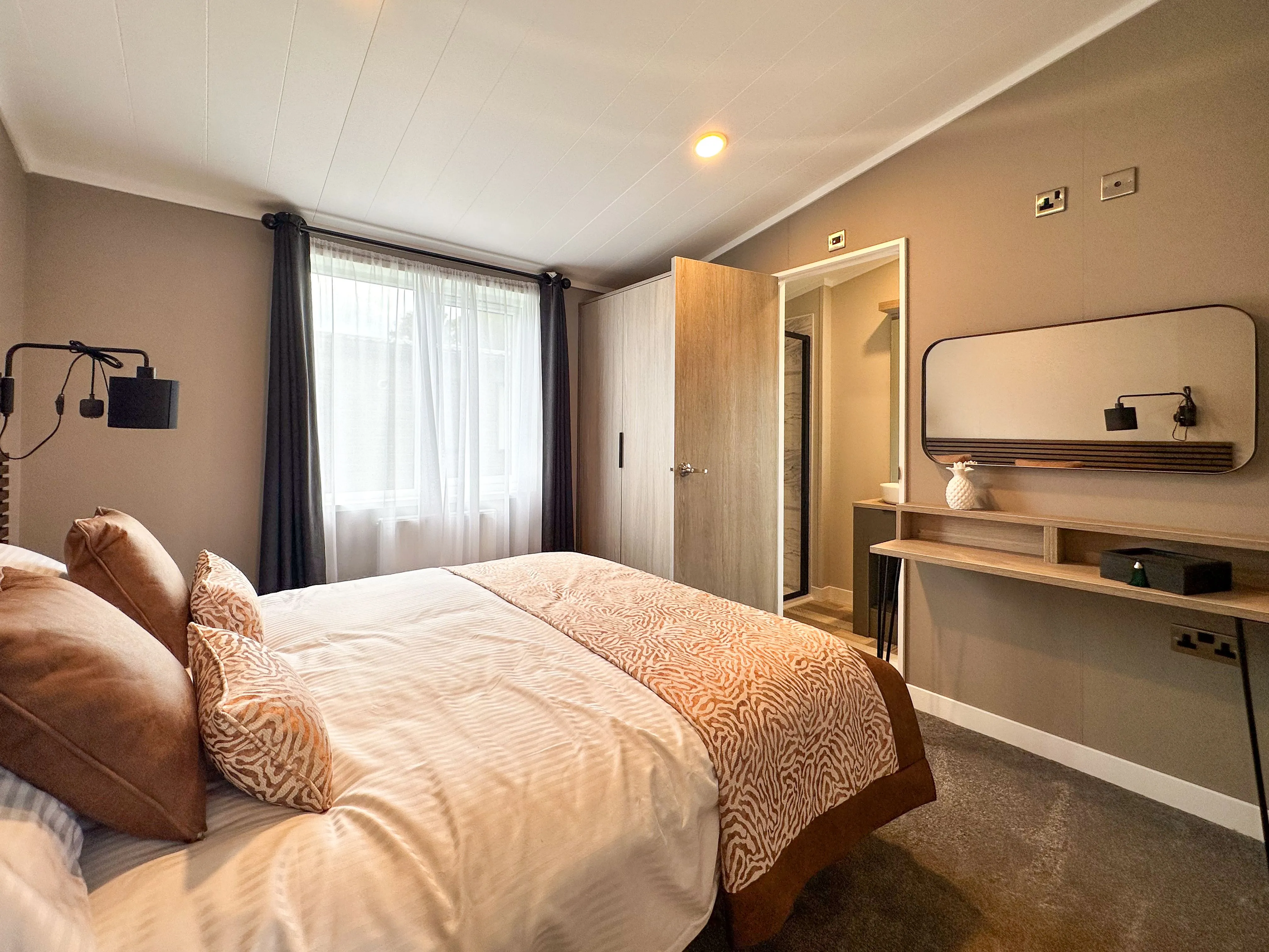 Modern bedroom with double bed, grey walls, window with dark curtains, and vanity desk with mirror