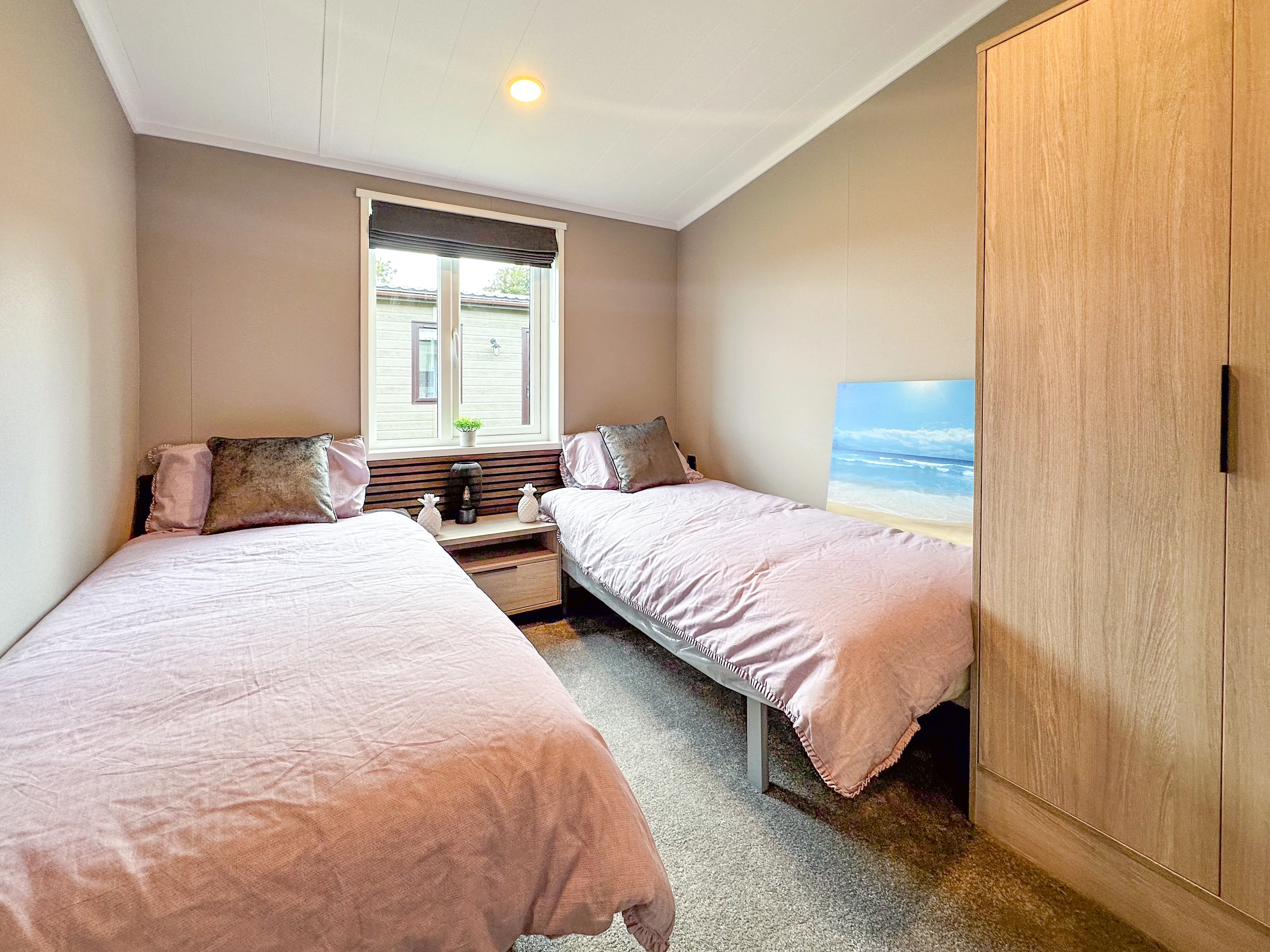 Small twin bedroom with two single beds in pale pink bedding, a central window and a wooden wardrobe