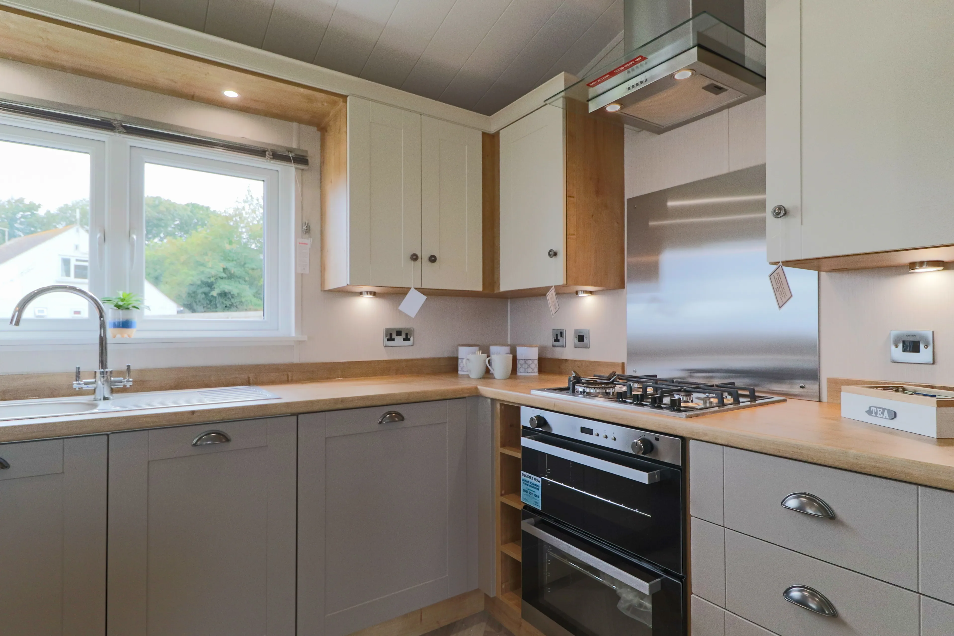 Modern fitted kitchen with grey cabinets, wooden worktops, window, sink and gas hob with oven