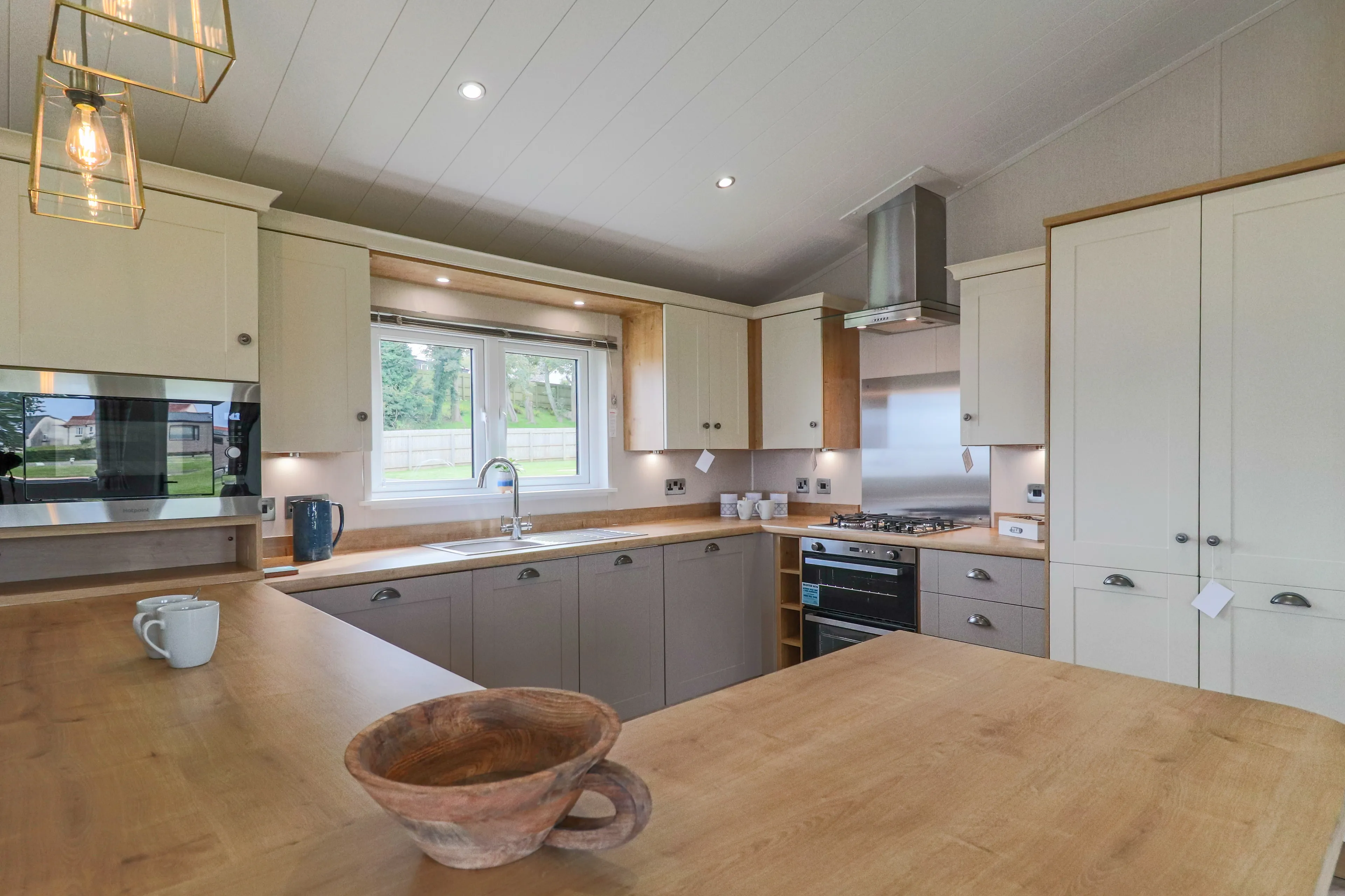 Modern fitted kitchen with wooden worktops, cream and grey cabinets, and a window above the sink