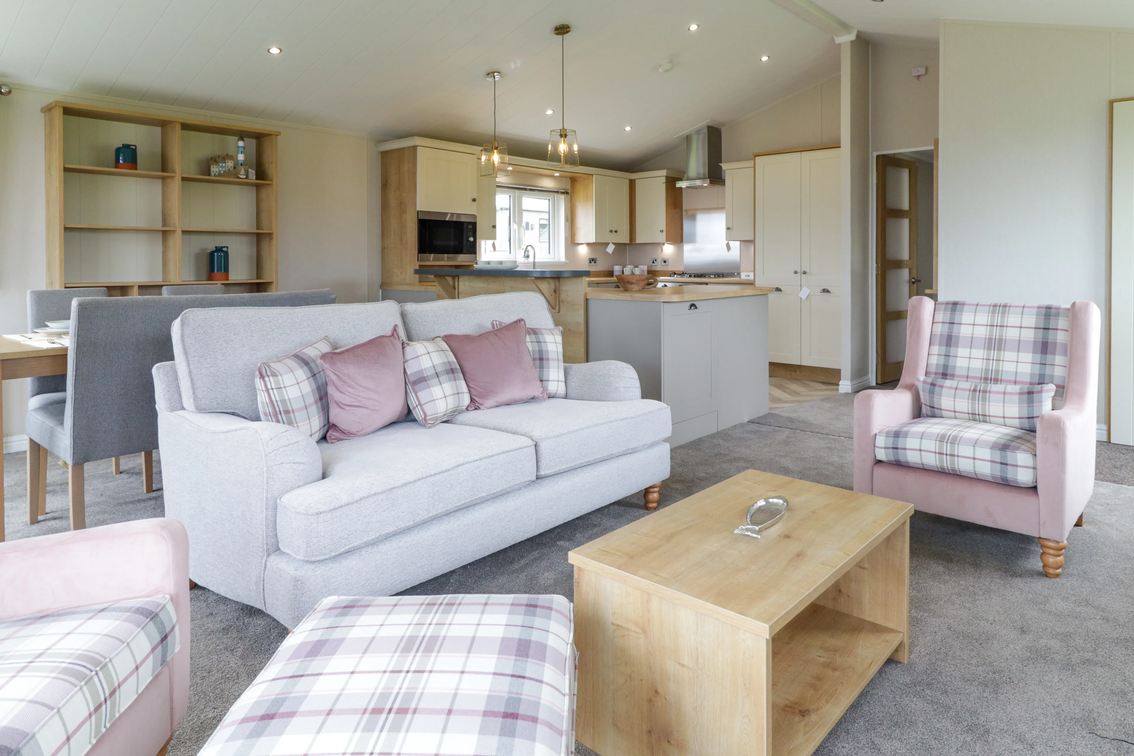 Modern open-plan living room and kitchen with grey sofa, pink plaid armchairs and wooden coffee table