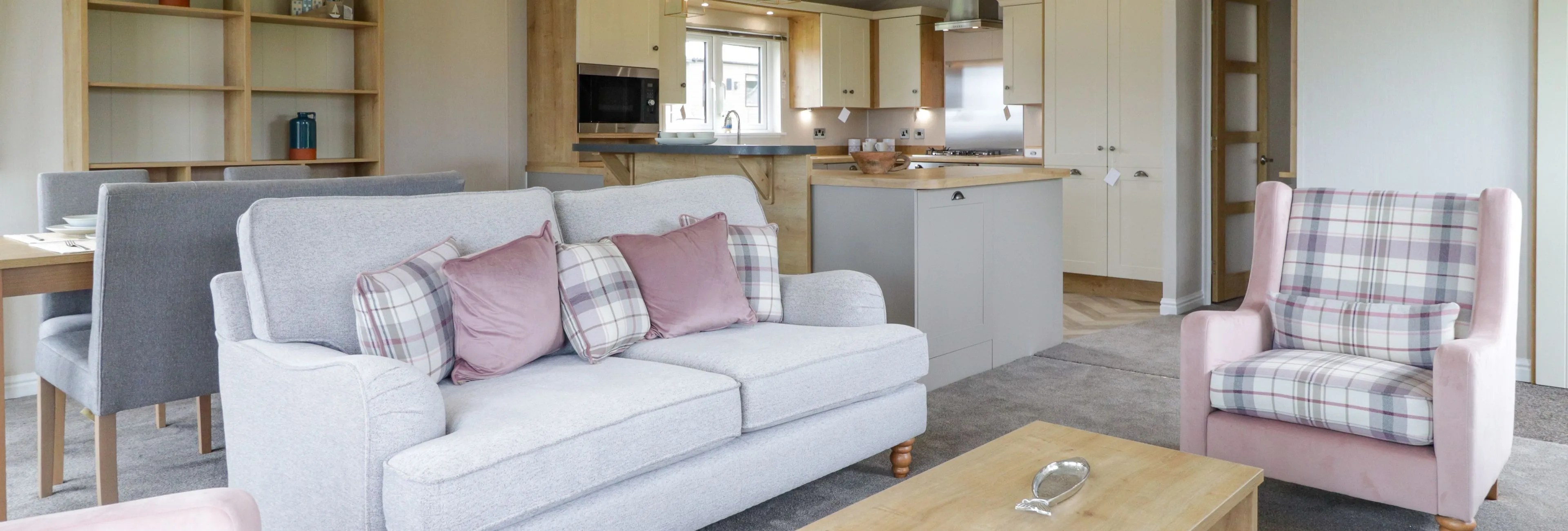 Modern open-plan living room and kitchen with grey sofa, pink plaid armchairs and wooden coffee table