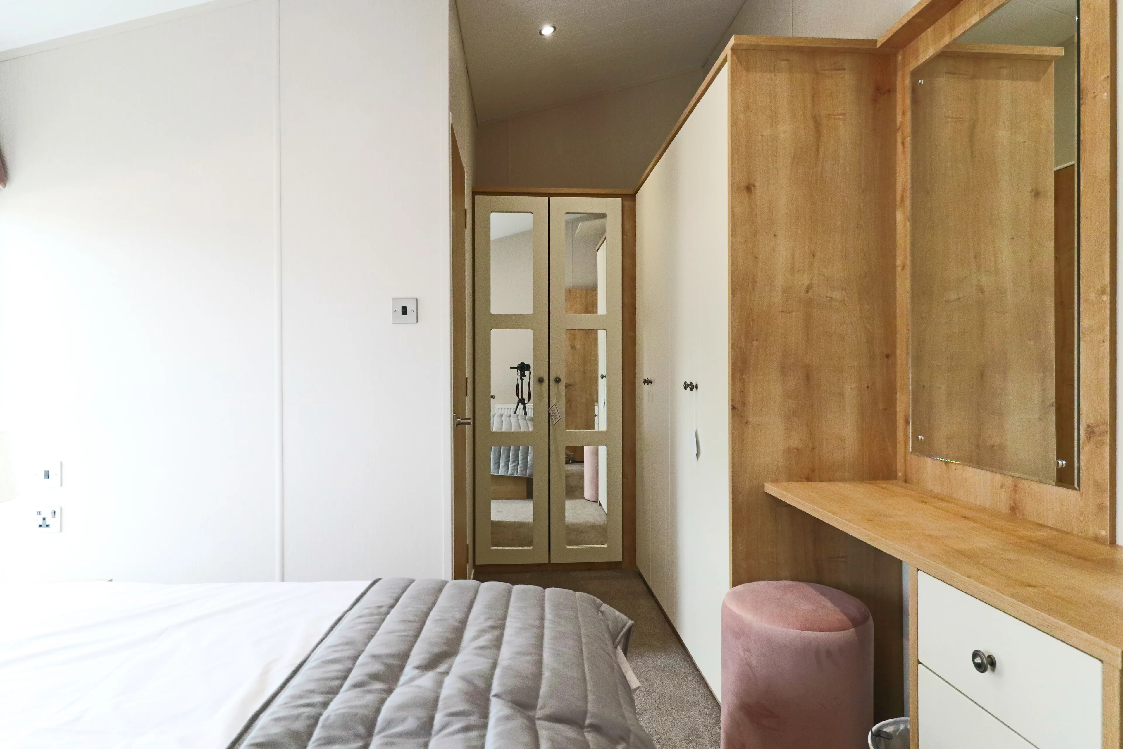Modern bedroom with mirrored wardrobe doors, built-in dressing table and pink stool