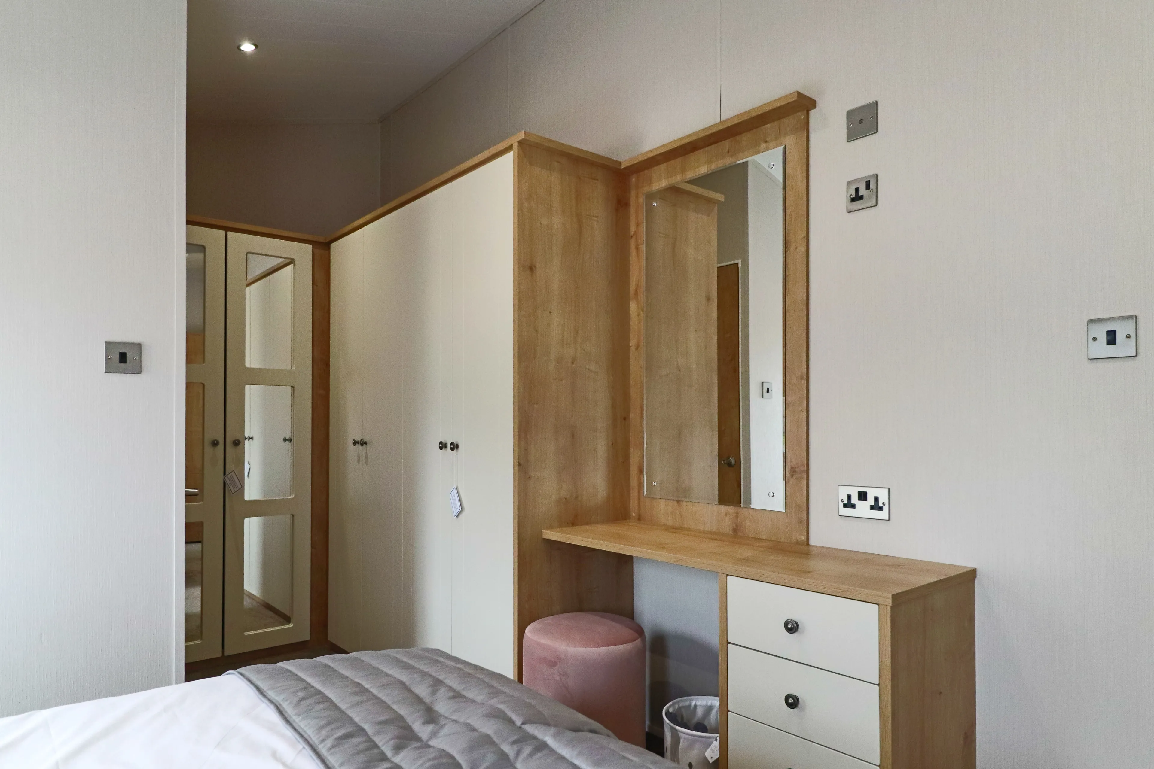Bedroom dressing area with wooden-framed mirror, vanity unit and cream wardrobes