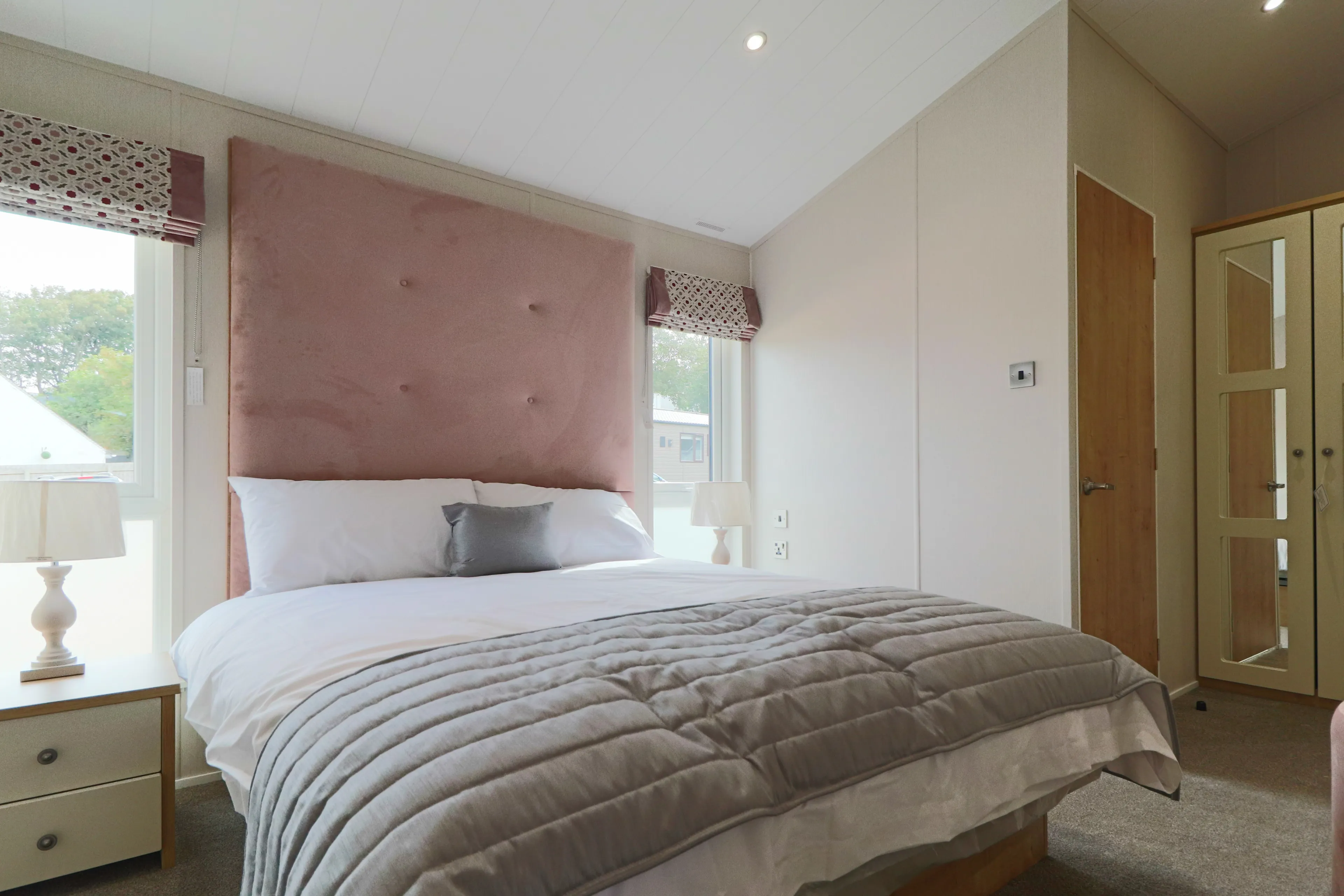 Bright bedroom with double bed, pink upholstered headboard, bedside lamps and mirrored wardrobe