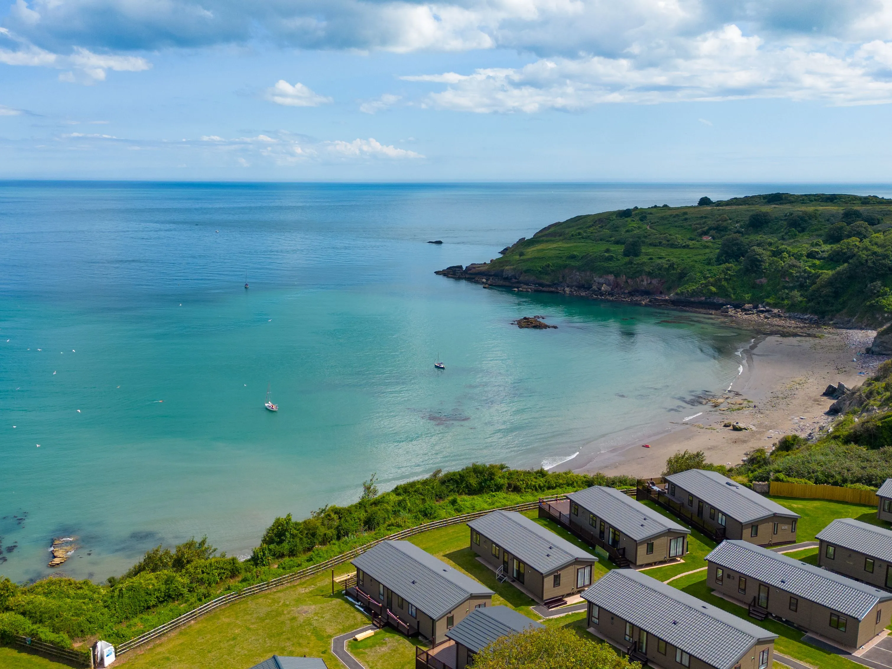 Aerial view of a turquoise bay with a sandy beach, small boats and coastal holiday lodges