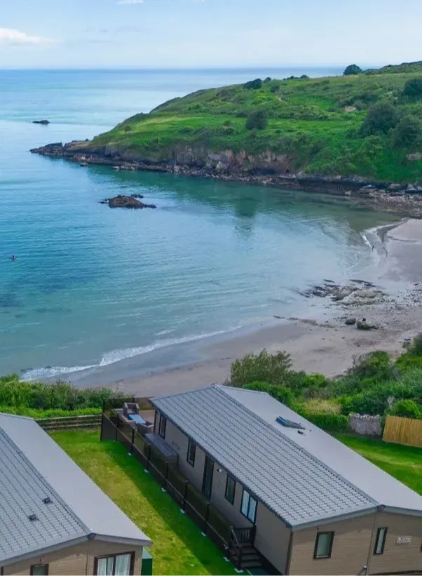 Coastal bay with sandy beach, calm sea and green headland, viewed above holiday lodges