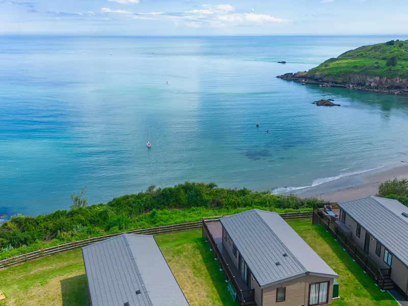 Coastal bay with calm blue sea, sandy beach, green headland and holiday lodges in the foreground