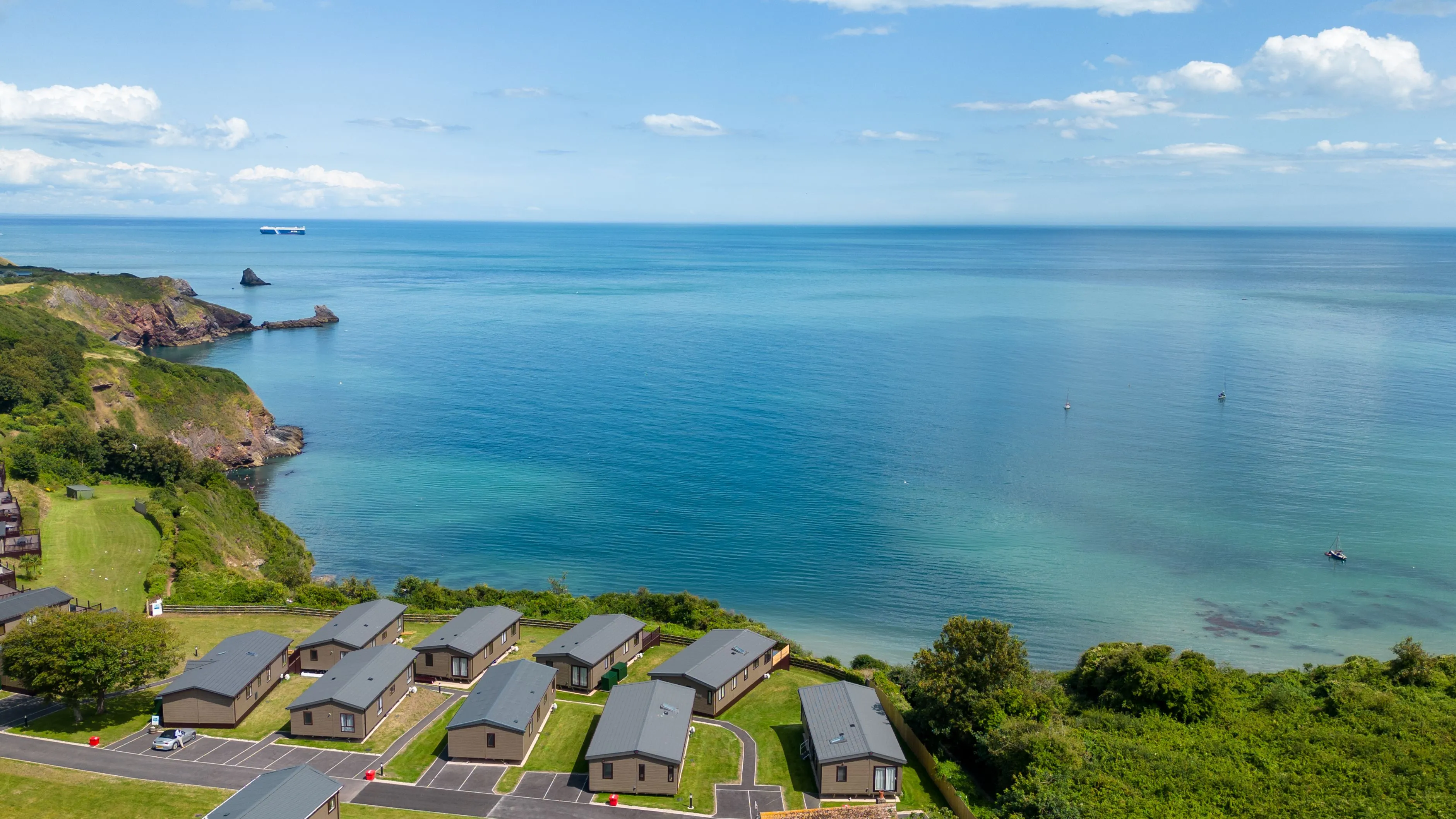 Coastal holiday park cabins overlooking a calm blue sea and rocky headland