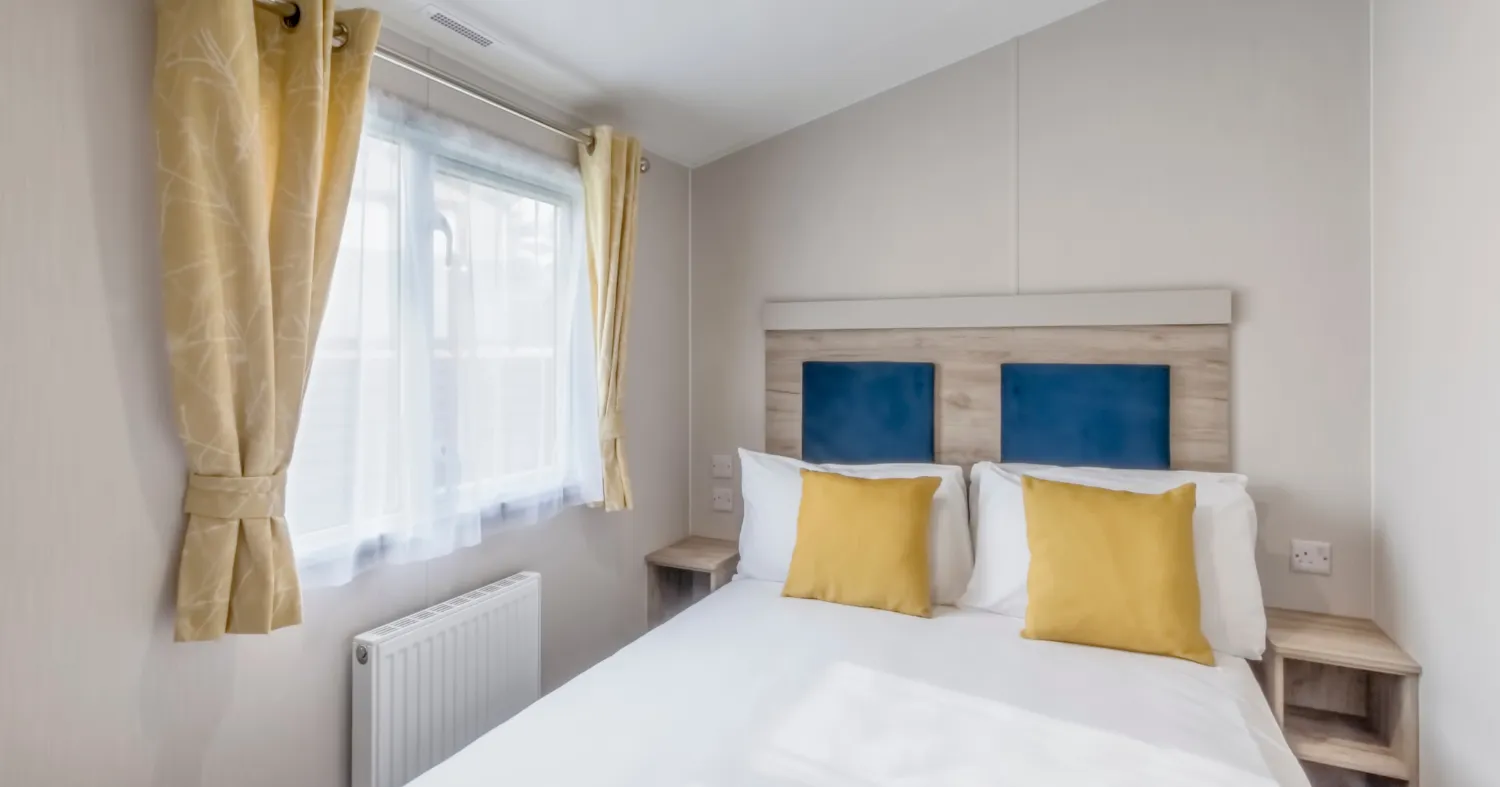 Bright double bedroom with white bedding, blue headboard panels and yellow cushions beside a window with yellow curtains.