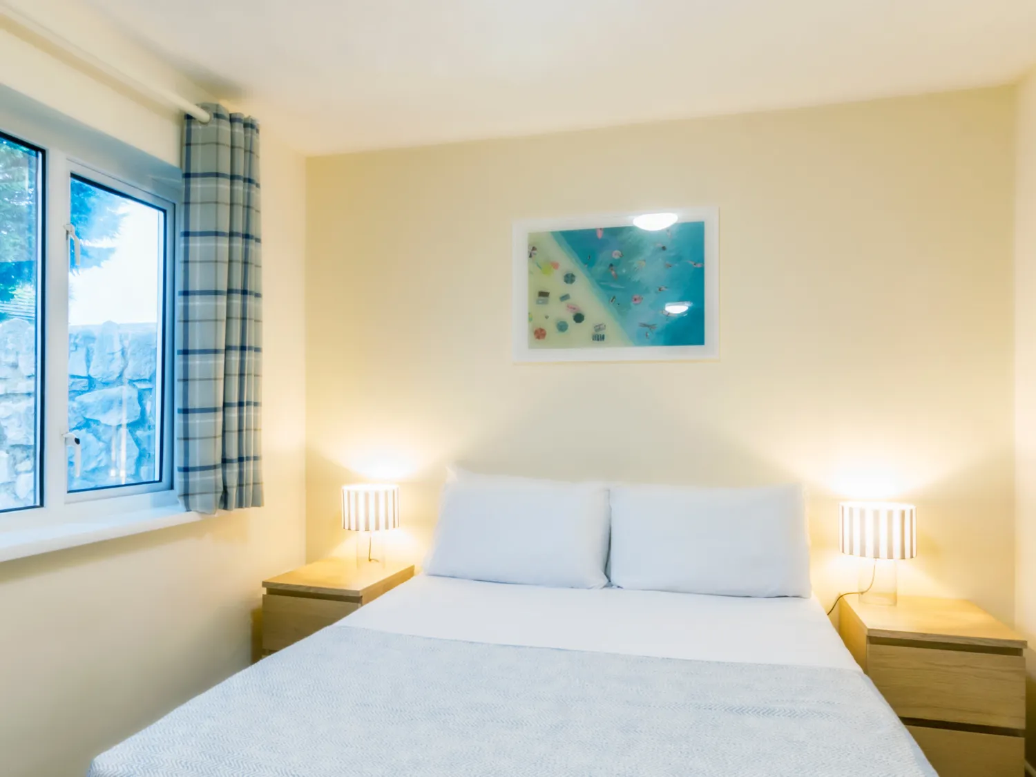Cosy bedroom with a double bed, bedside lamps and a window with checked curtains