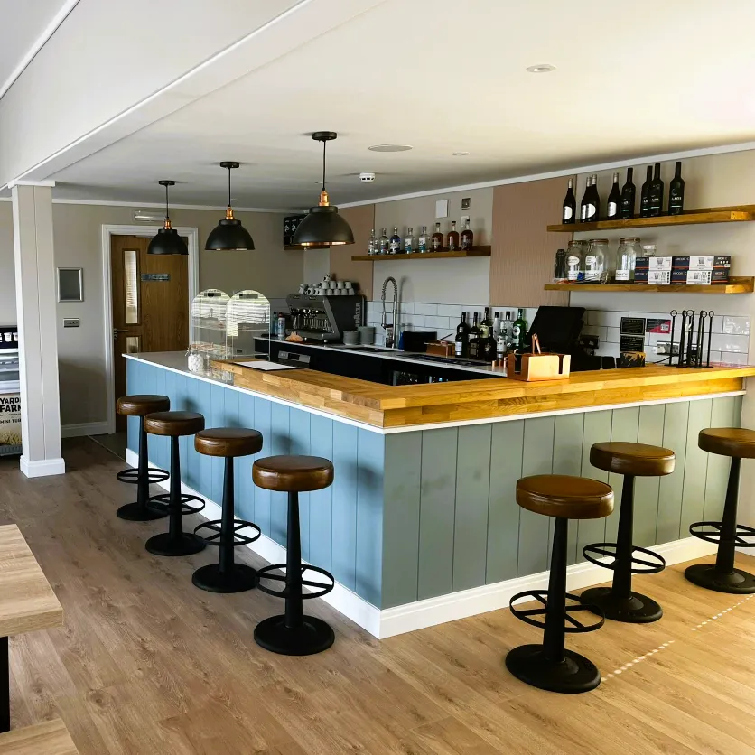 Modern bar interior with wooden countertop, pastel panelled bar front and leather bar stools under pendant lights