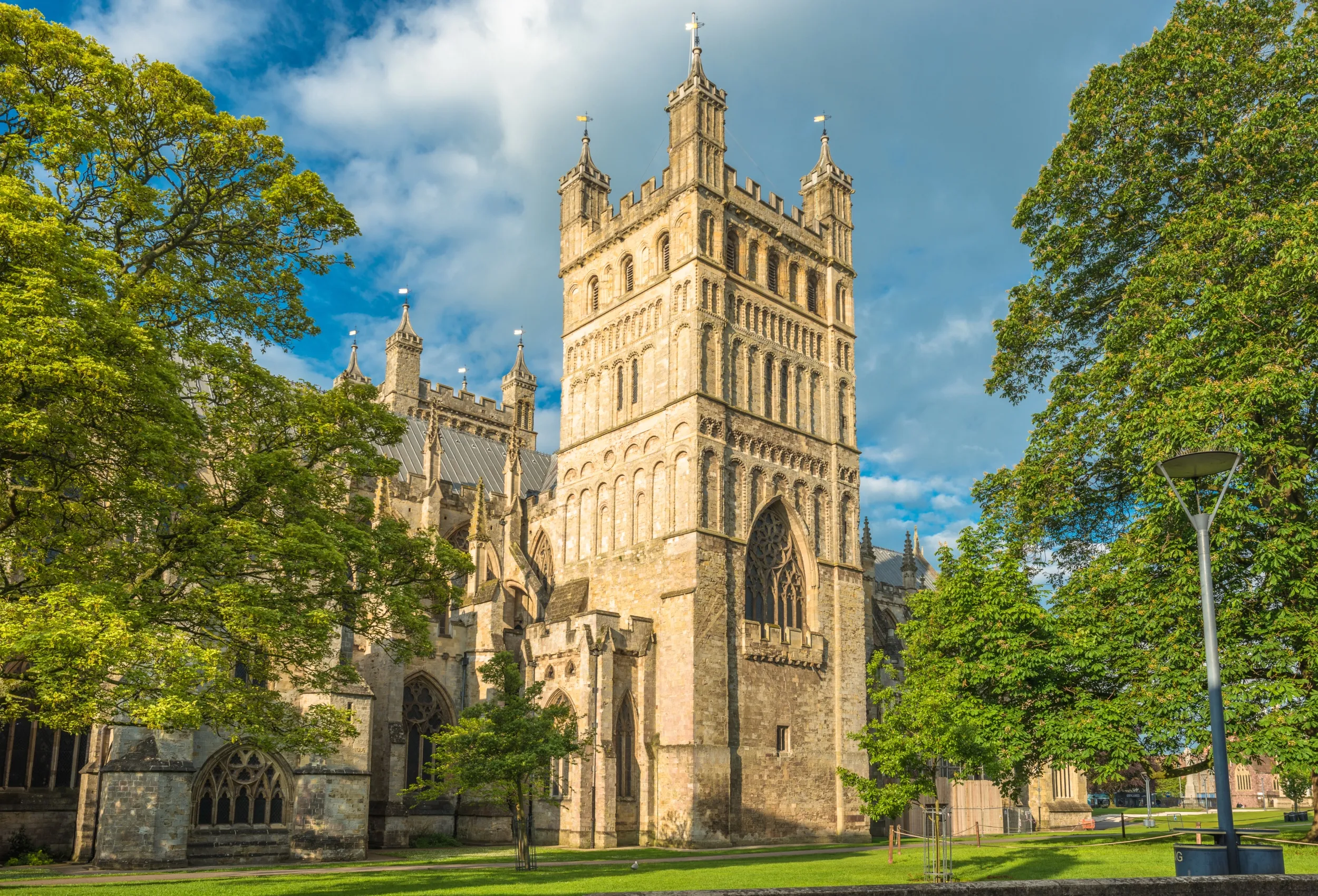 Stone cathedral tower framed by green trees under a blue sky