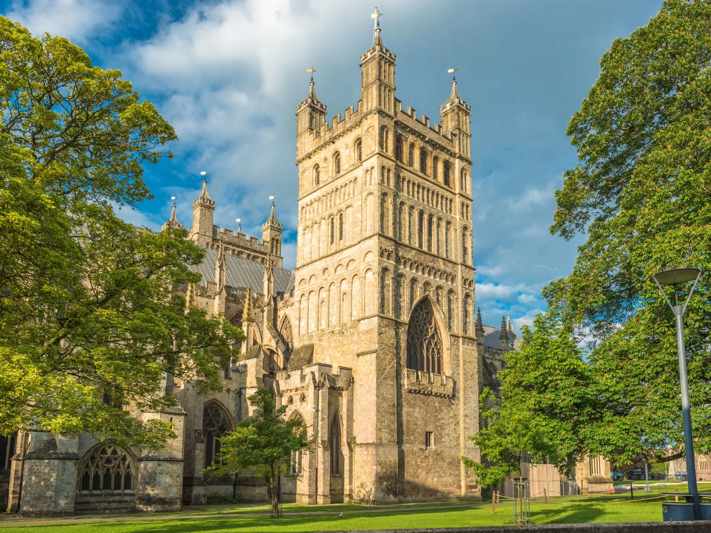 Stone cathedral tower framed by green trees under a blue sky