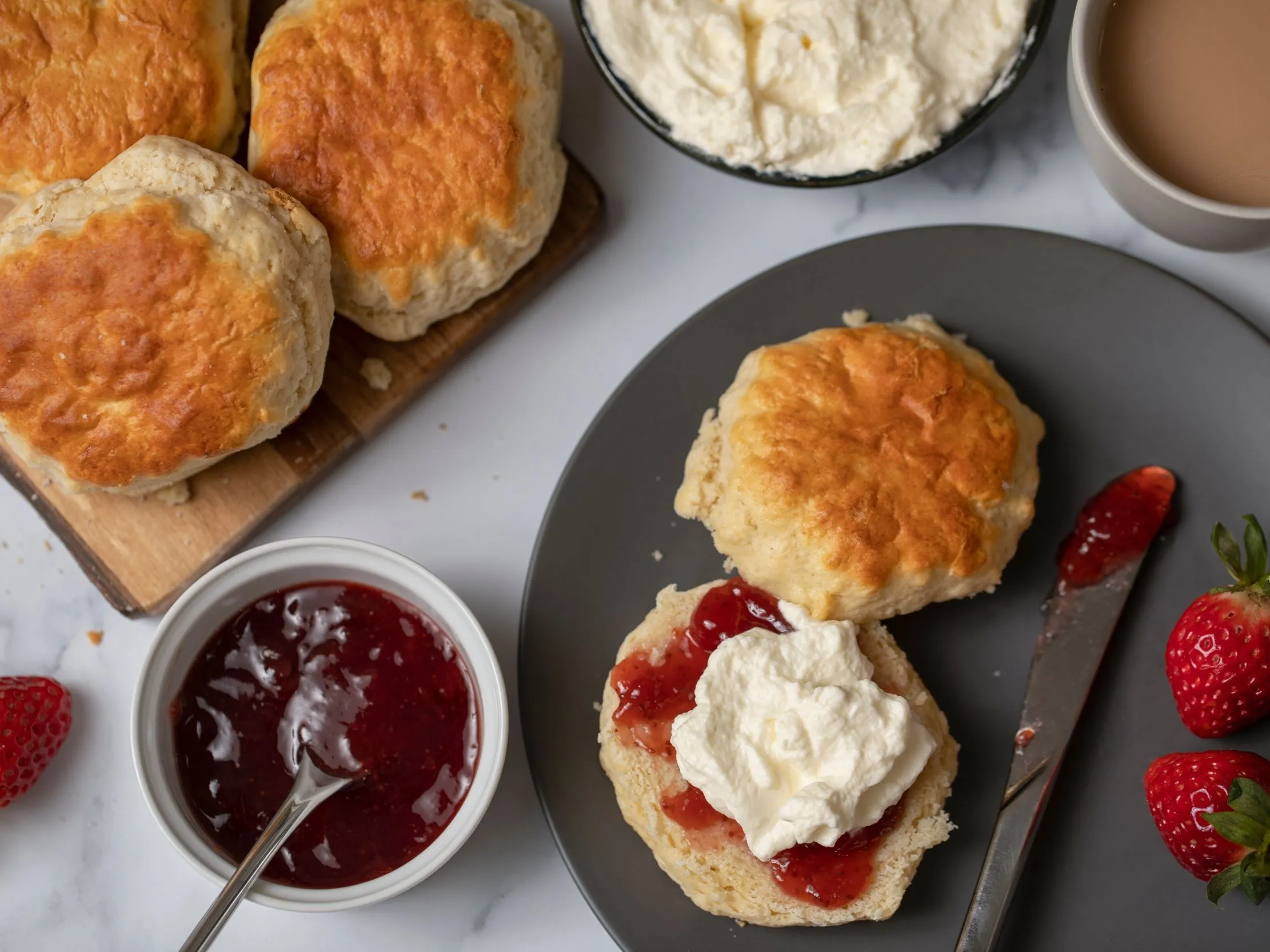 Freshly baked scones with strawberry jam and clotted cream on a plate with tea