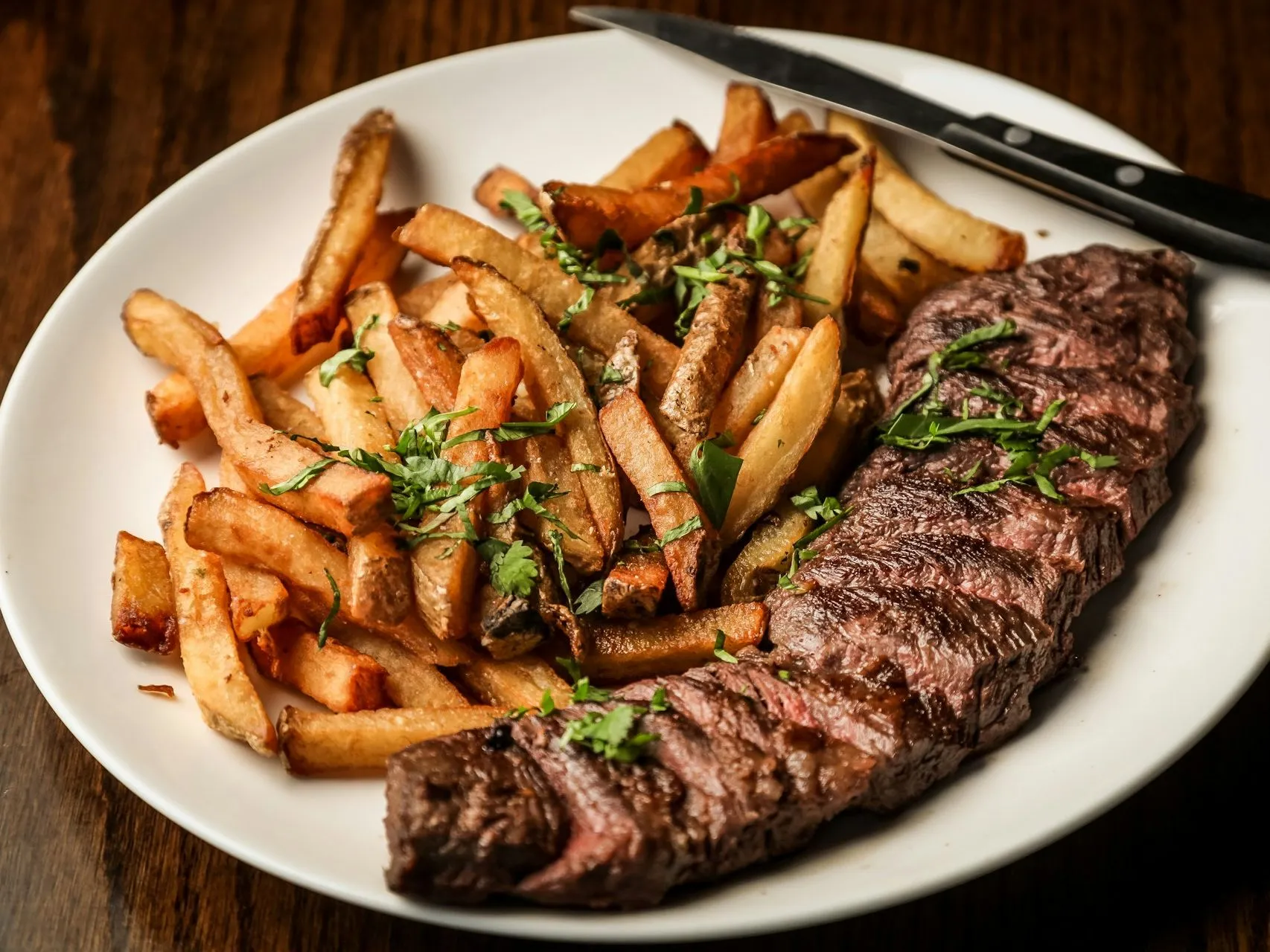 Plate of steak and chips with chopped herbs on a wooden table