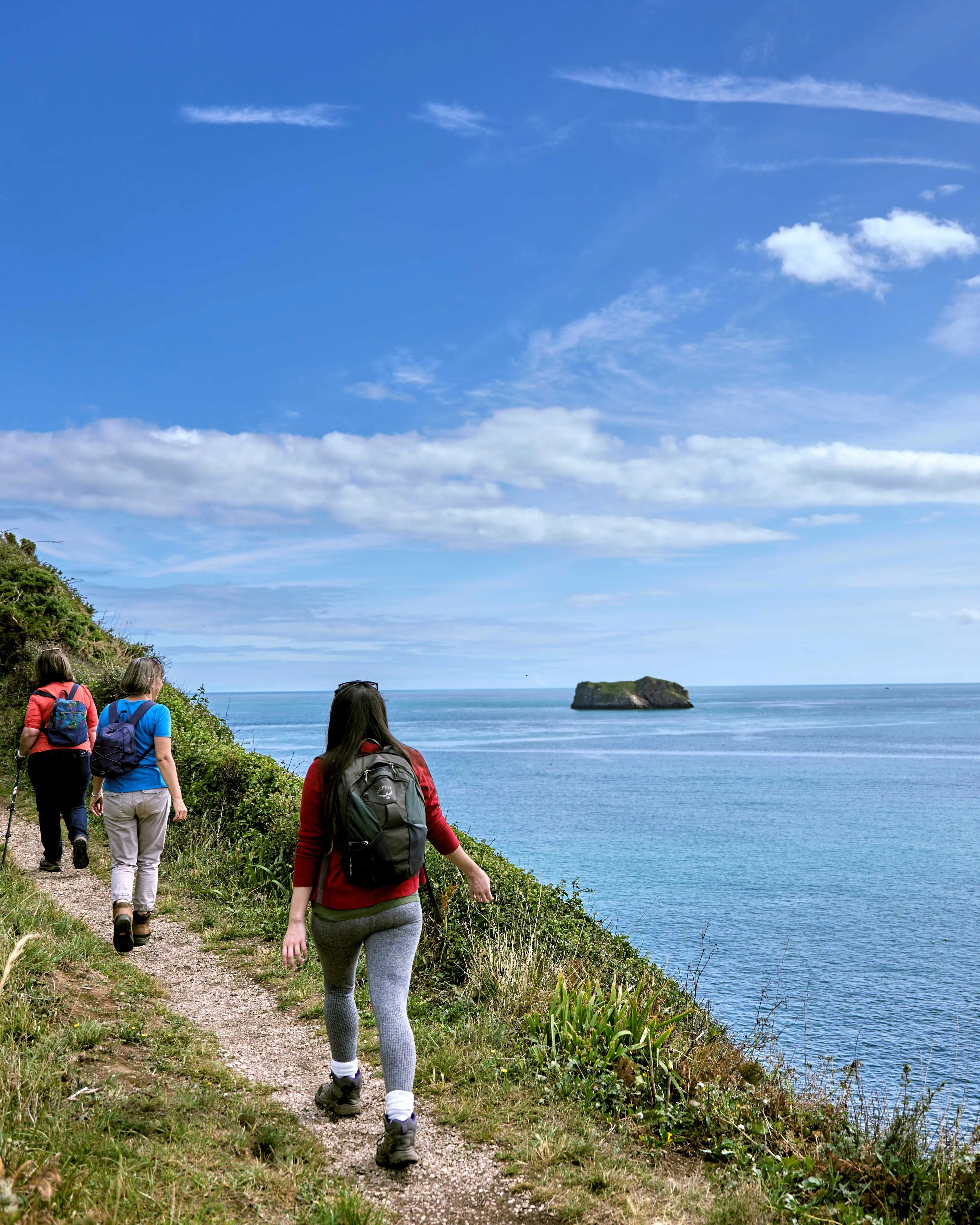 Walkers with backpacks on a coastal cliff path overlooking the sea under a blue sky