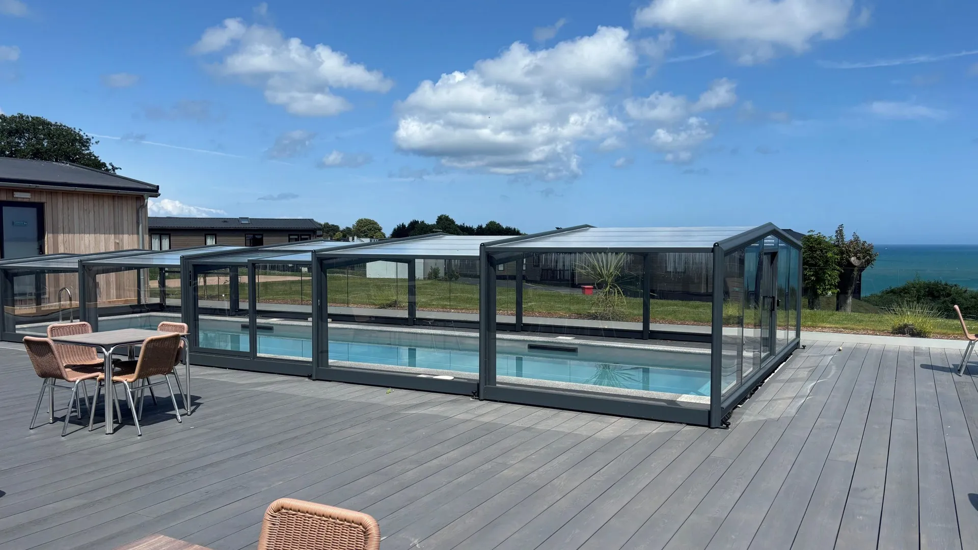 Outdoor swimming pool under a glass enclosure on a grey deck with sea view