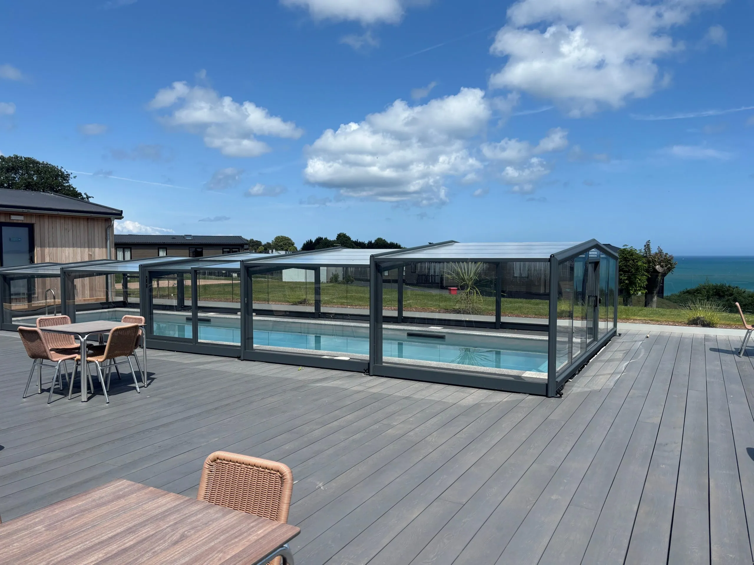 Outdoor swimming pool under a glass enclosure on a grey deck with sea view