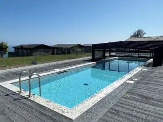 Outdoor swimming pool with retractable cover beside modern lodges overlooking the sea