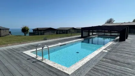 Outdoor swimming pool with retractable cover beside modern lodges overlooking the sea