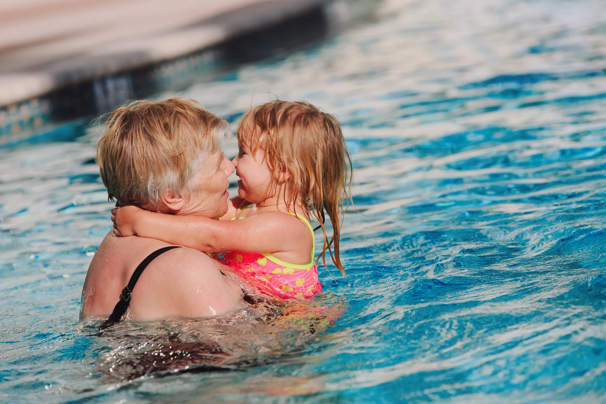 Older woman holding and cuddling a young girl in a swimming pool