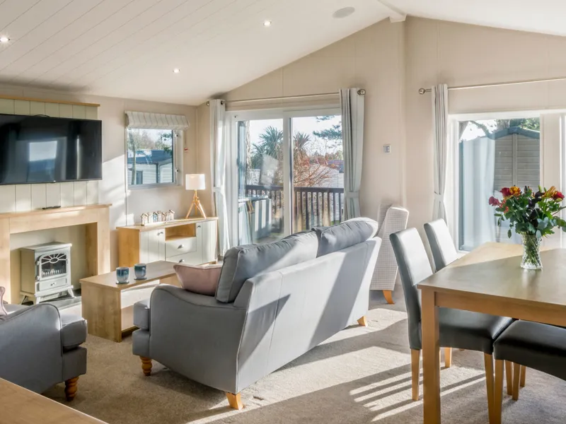 Bright, spacious lounge and dining area inside Landscove Lodge with grey sofas, a fireplace, large windows and patio doors.