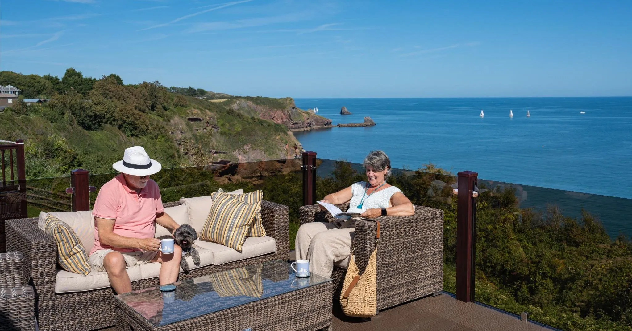 Mature couple relaxing on a cliff-top decking terrace in Devon with sea views and their dog
