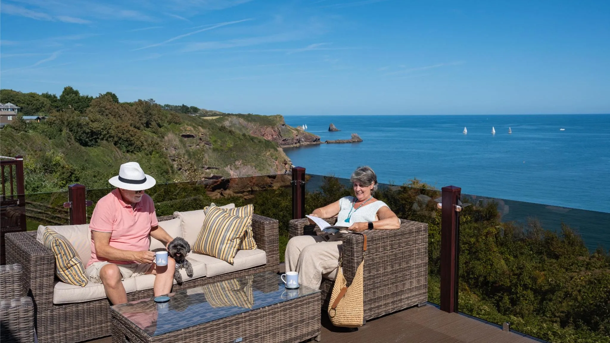 Mature couple relaxing on a cliff-top decking terrace in Devon with sea views and their dog