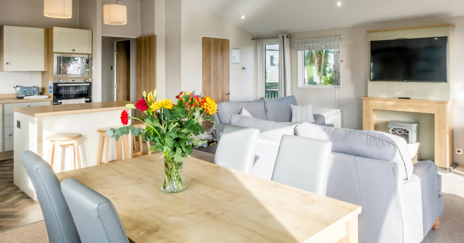 Open-plan dining area and lounge in Landscove Lodge with a wooden table, grey chairs, kitchen breakfast bar and bright modern interior