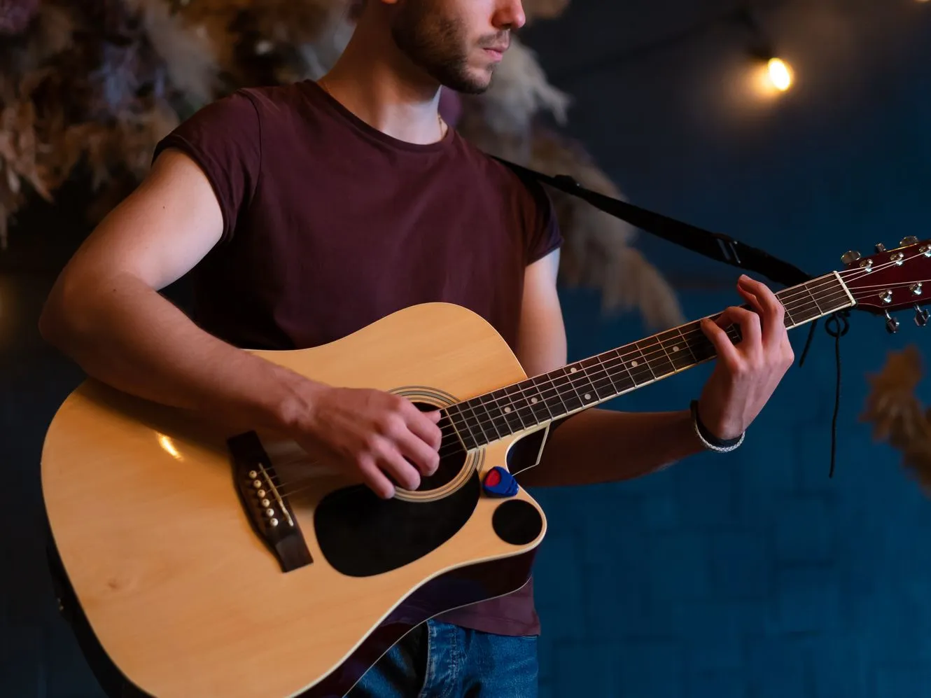 Young man playing an acoustic guitar under warm hanging lights indoors