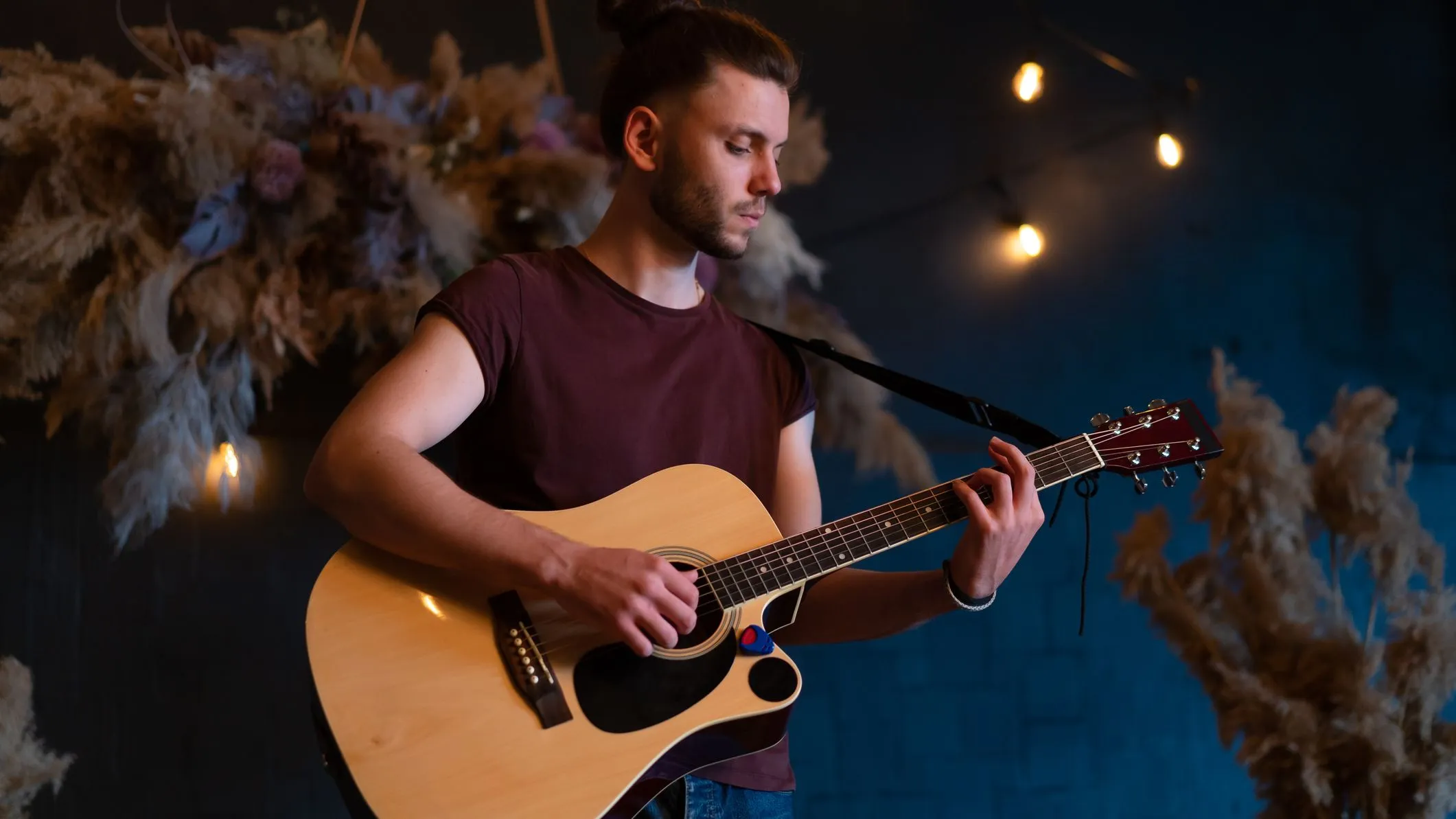 Young man playing an acoustic guitar under warm hanging lights indoors