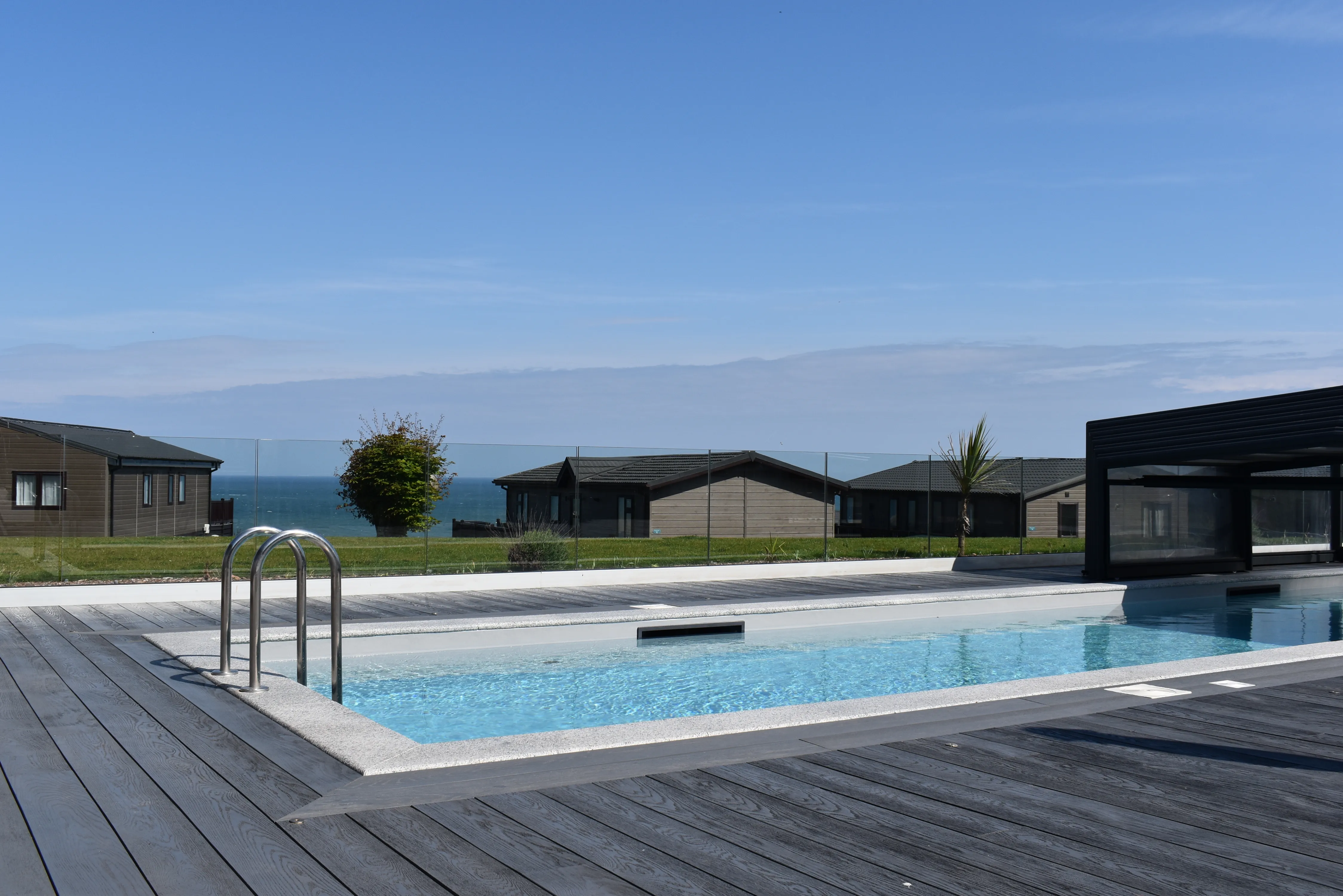 Outdoor swimming pool with wooden decking and sea views beside modern holiday lodges