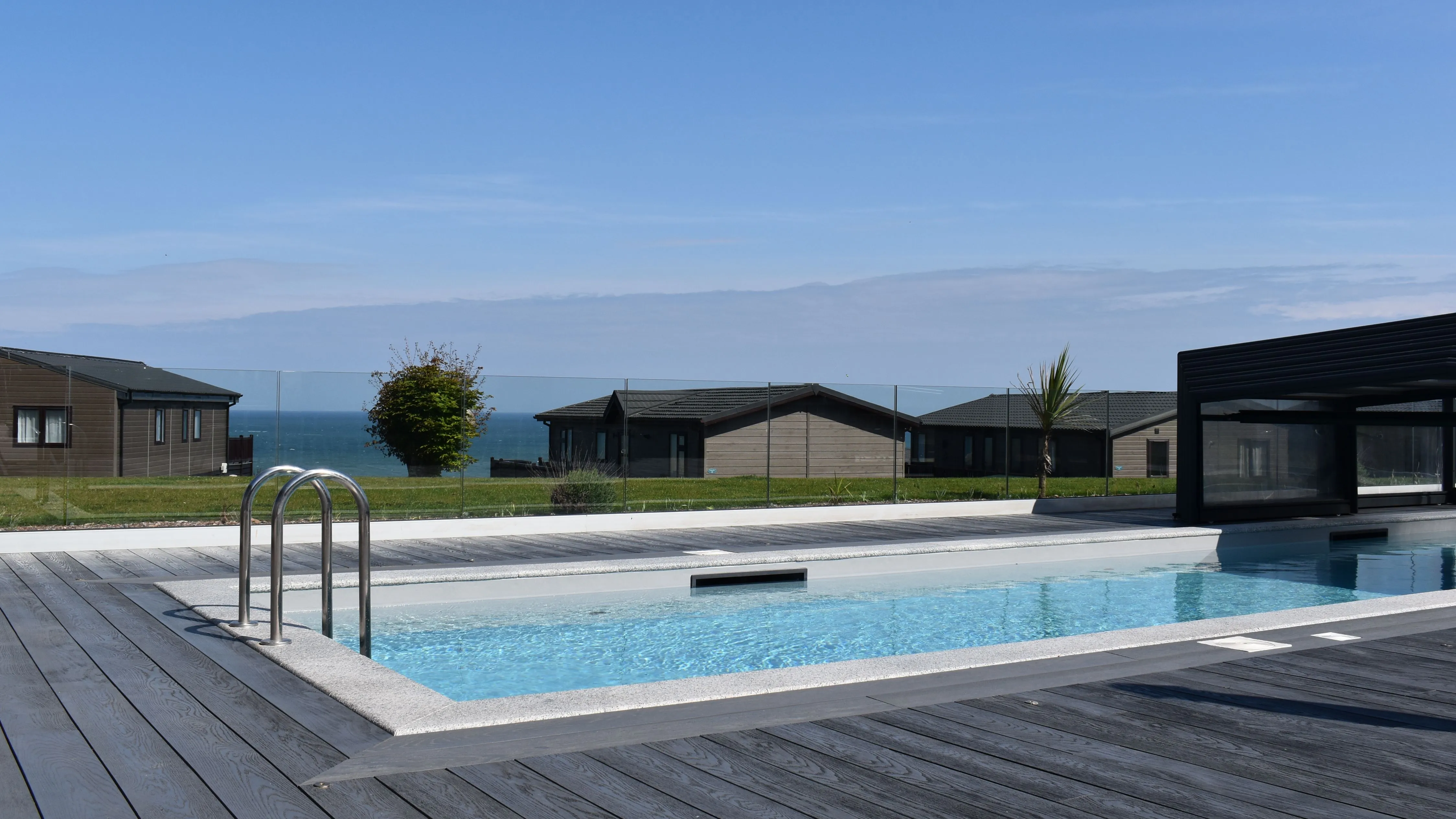 Outdoor swimming pool with wooden decking and sea views beside modern holiday lodges