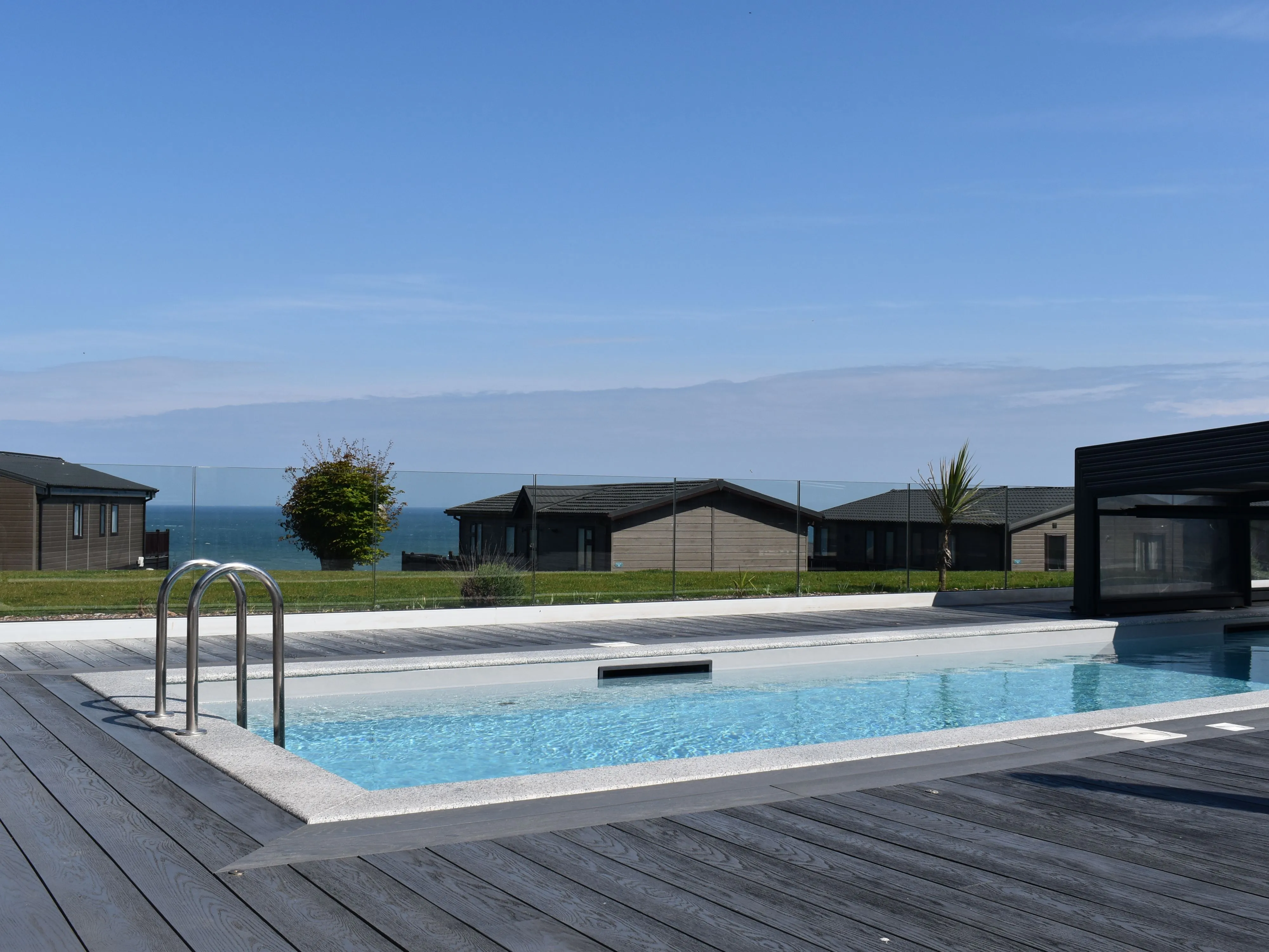Outdoor swimming pool with wooden decking and sea views beside modern holiday lodges