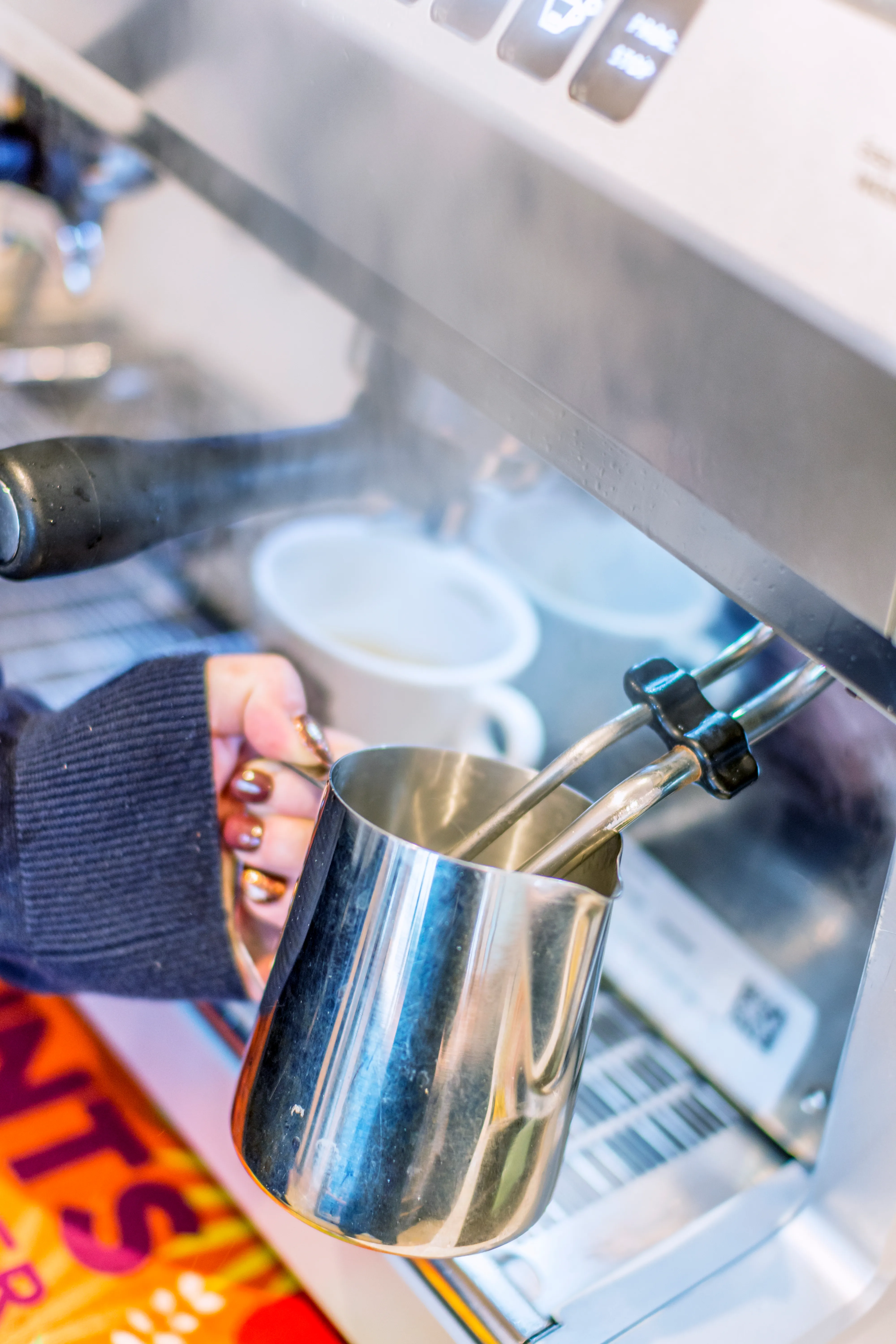Close-up of a person steaming milk with a metal jug using an espresso machine.