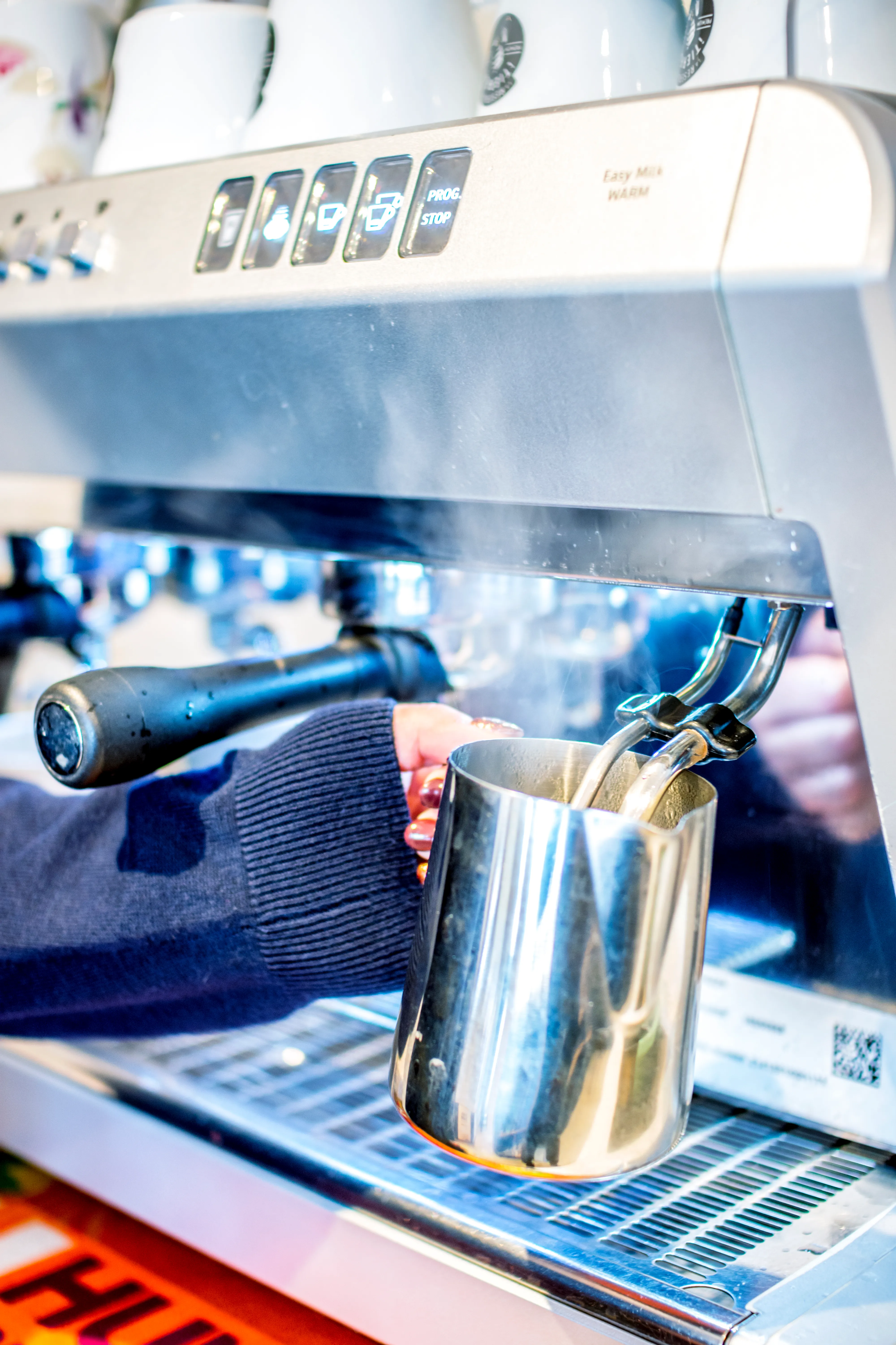 Close-up of a barista steaming milk in a metal jug with a commercial espresso machine.