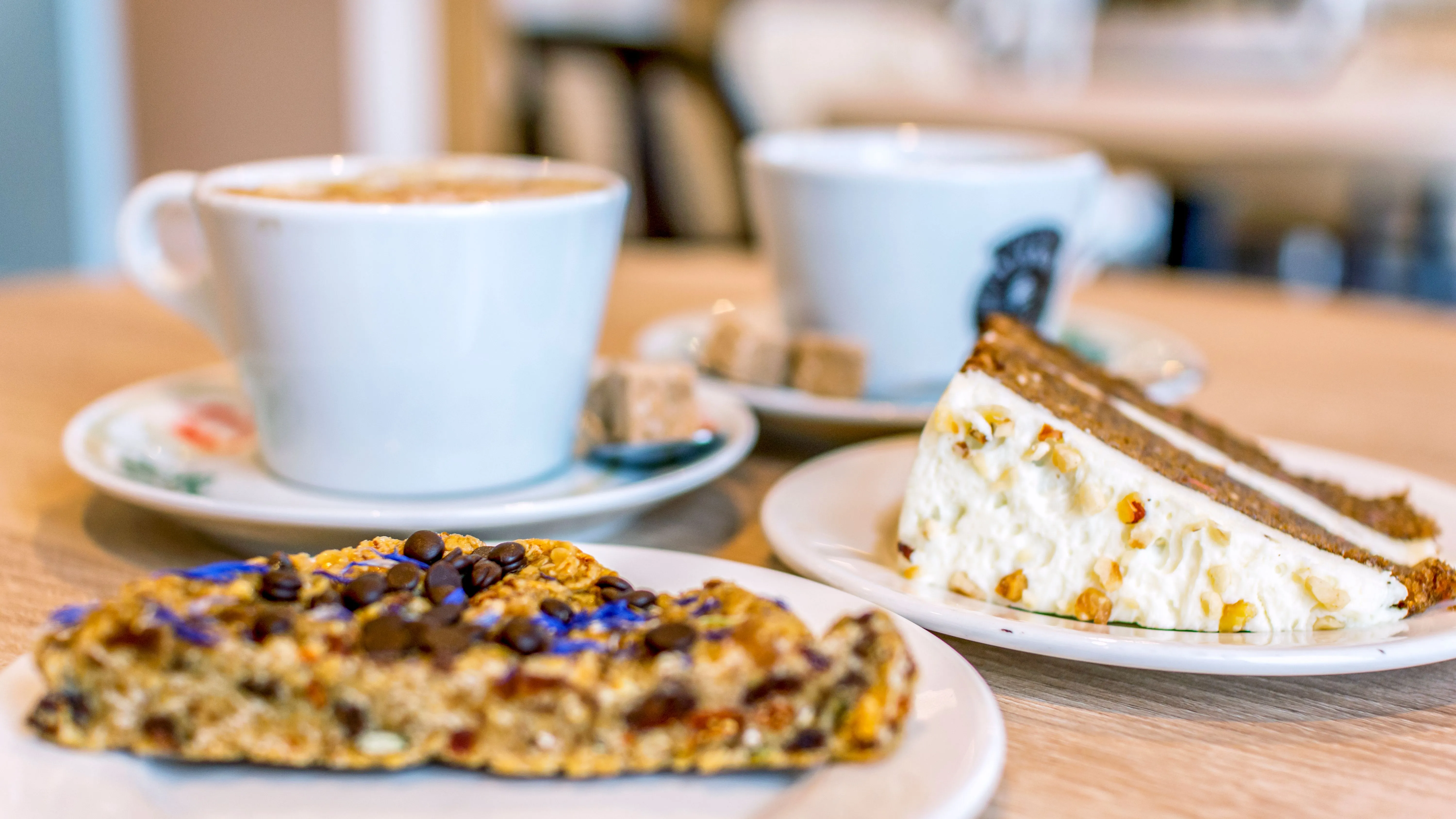Two cups of coffee served with a slice of cake and a biscuit on a café table.