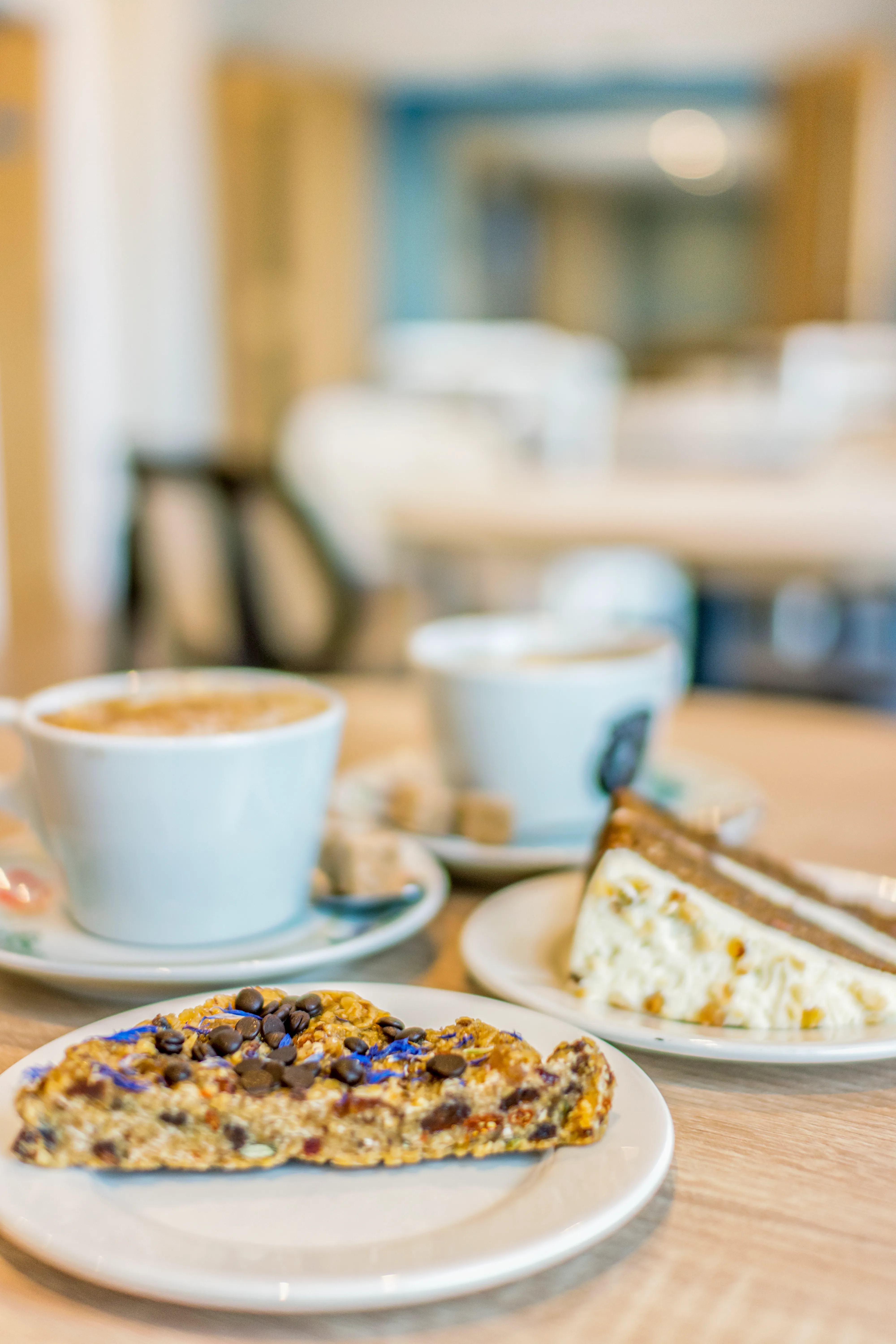Coffee and cake on a café table with a biscuit in the foreground