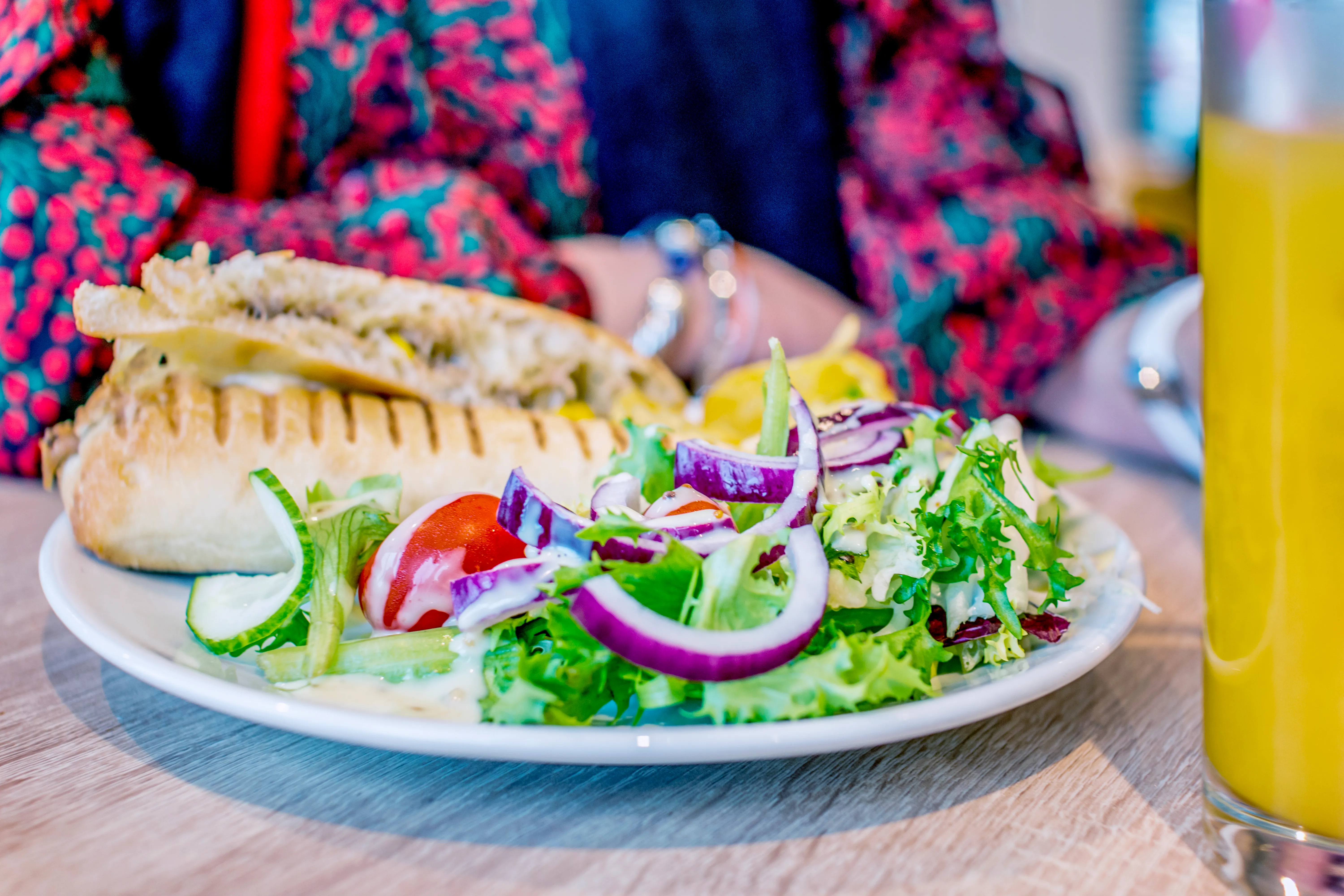Toasted sandwich with a fresh side salad and a glass of orange juice on a café table
