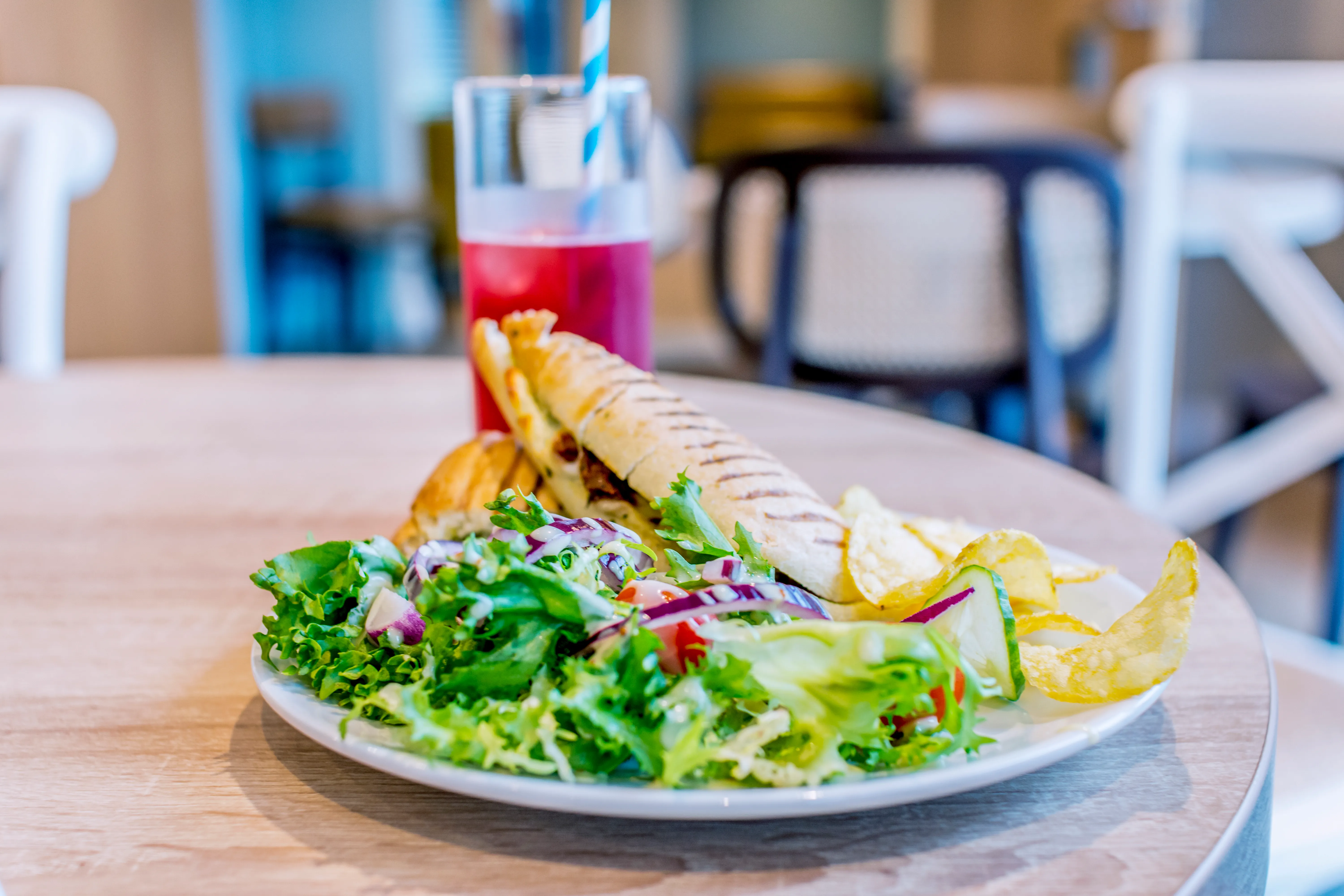 Grilled panini served with a fresh mixed salad, crisps and a pink drink on a café table