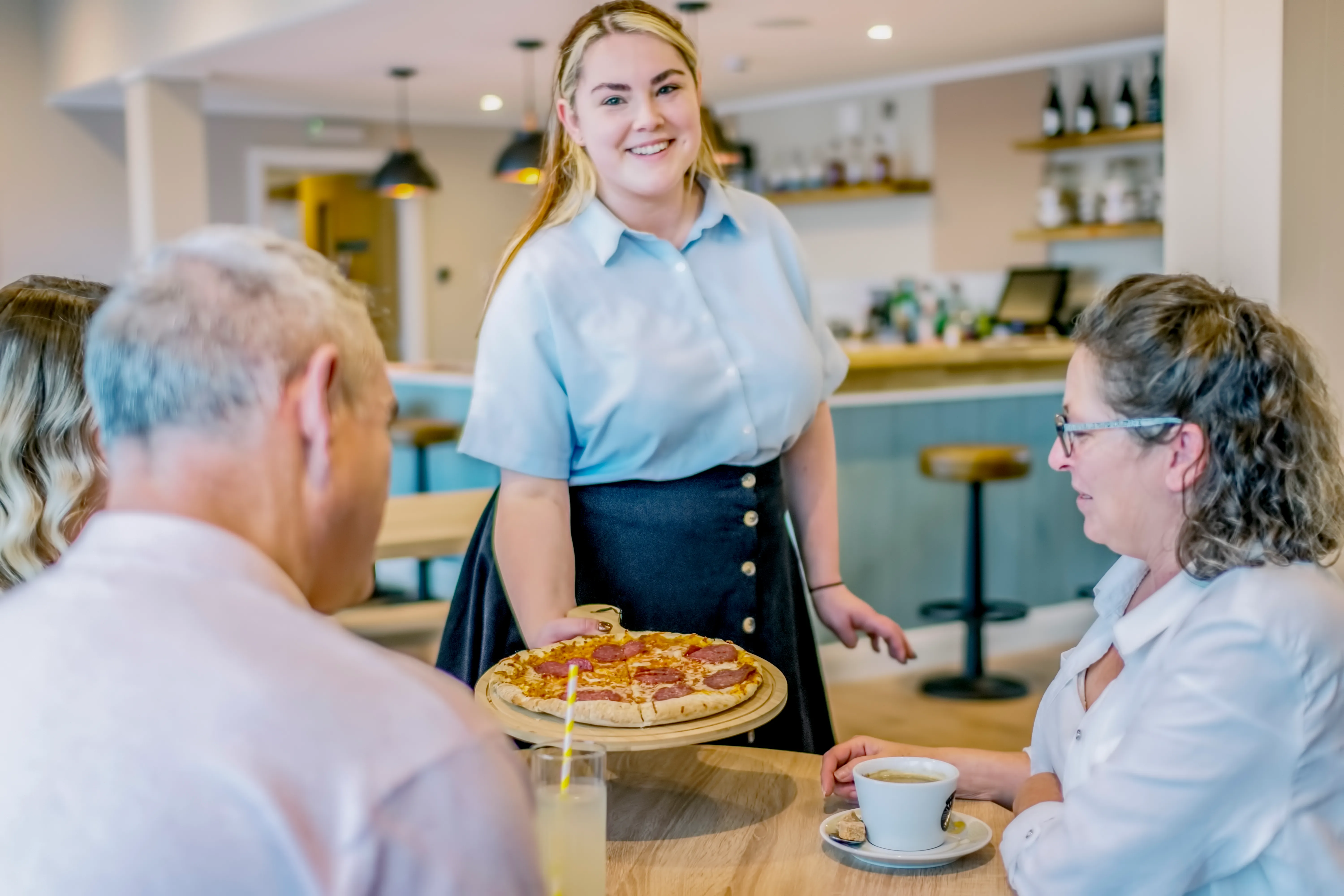 Waitress serving a pizza to customers seated at a café table