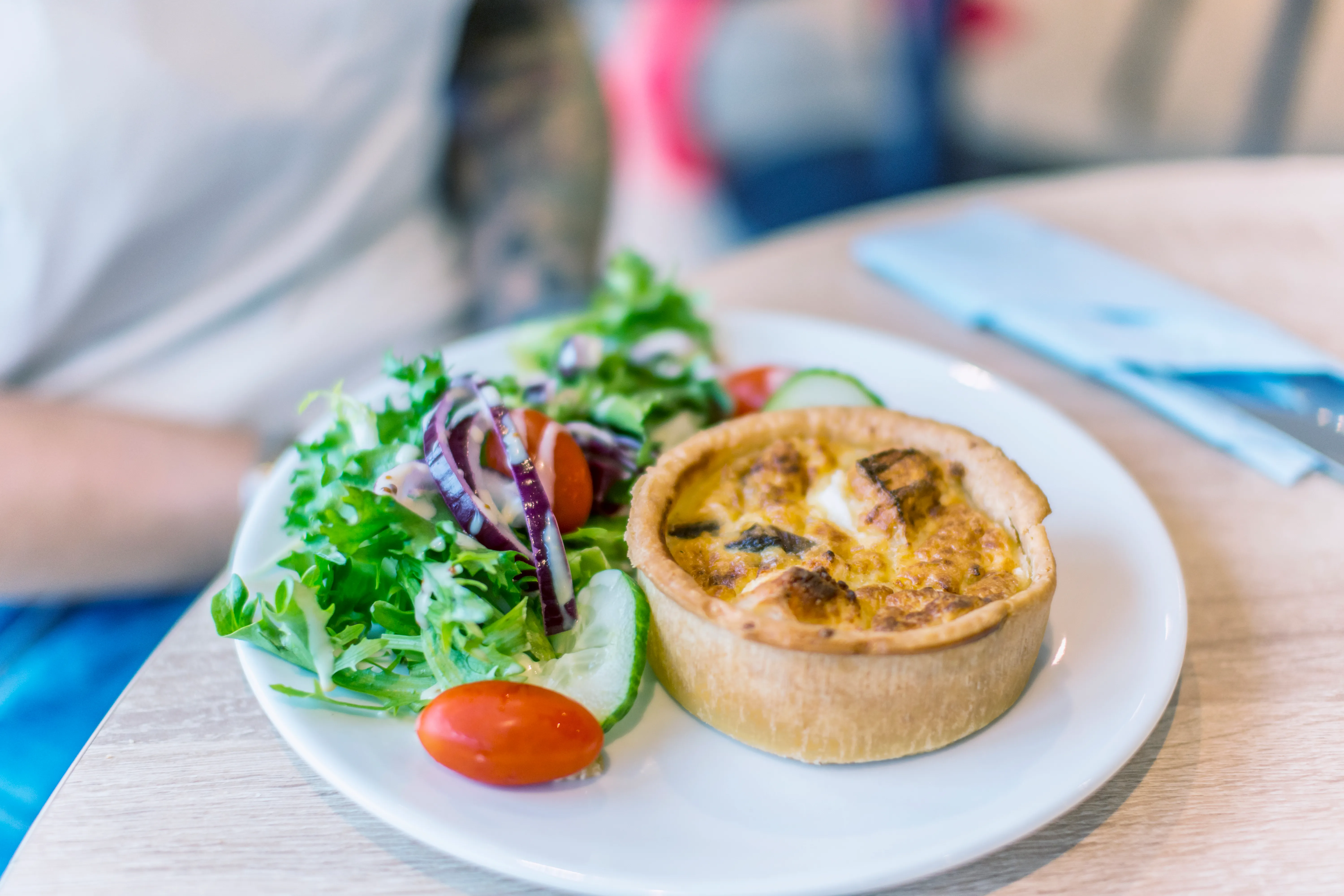 A savoury quiche served with a fresh side salad of lettuce, red onion, cucumber and cherry tomatoes on a white plate.