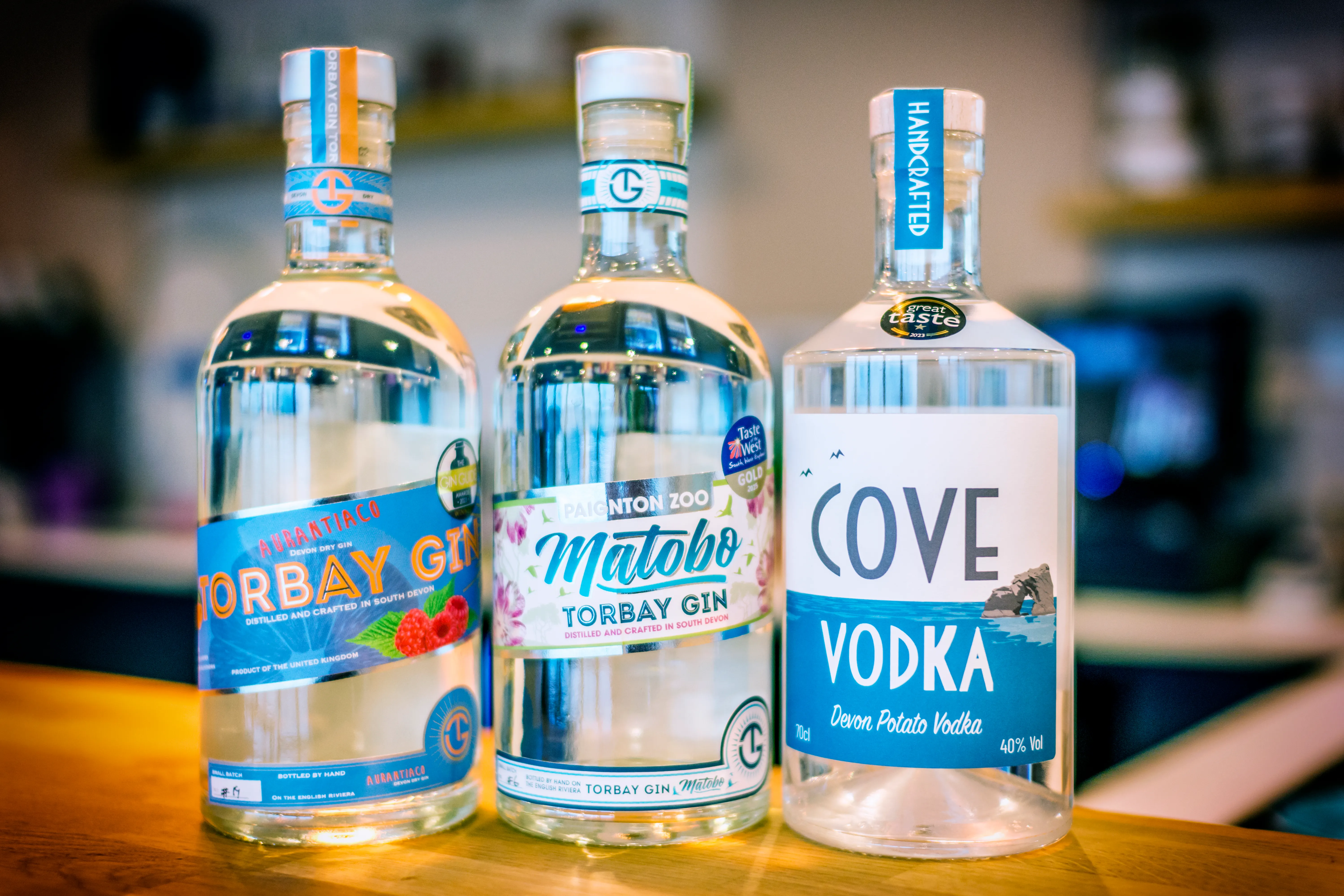 Three bottles of locally crafted spirits on a wooden bar: Torbay Gin Aurantiaco, Matobo Torbay Gin and Cove Vodka.